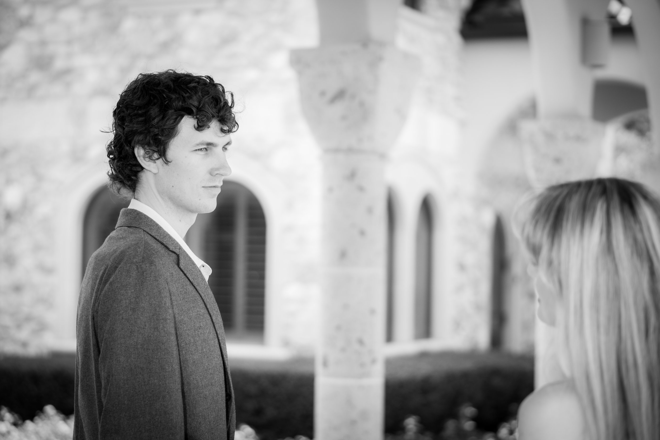 A young man and woman having a conversation outdoors in front of a stone building with arched windows.