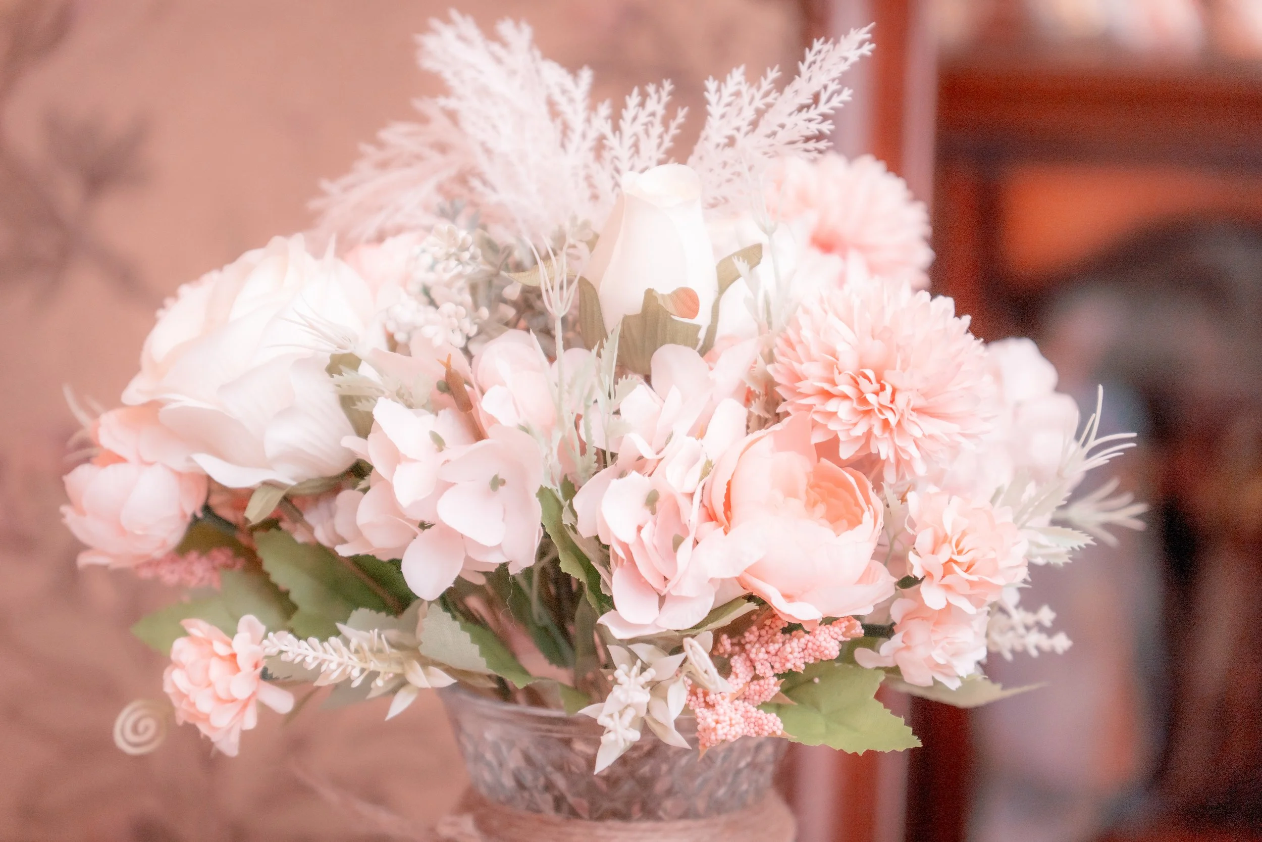 A bouquet of light pink and white flowers with green leaves in a glass vase.