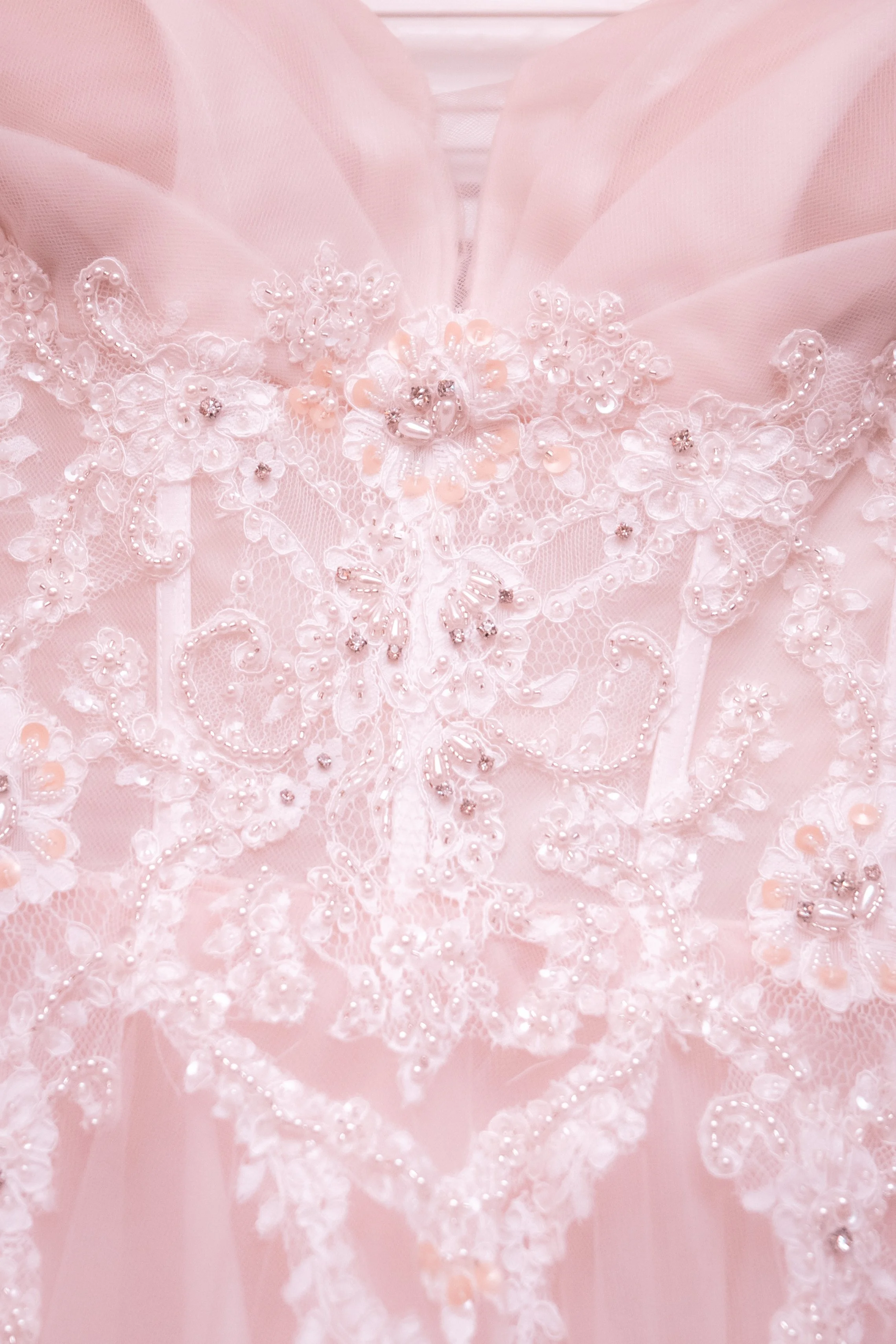 Close-up of a pink fabric with intricate floral embroidery and beadwork, likely part of a dress or garment.