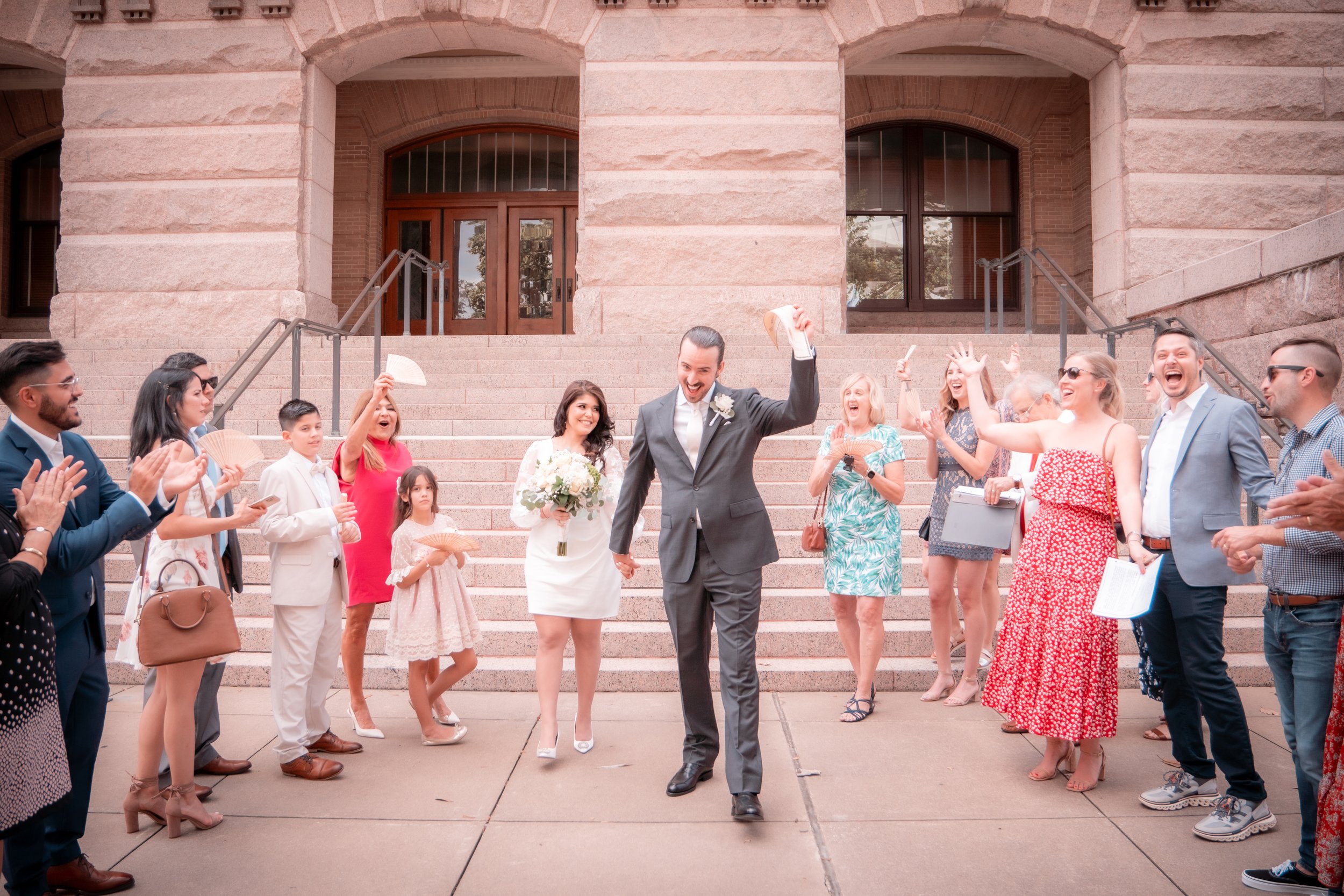 Couple in wedding attire holding hands walking down steps while guests celebrate around them.
