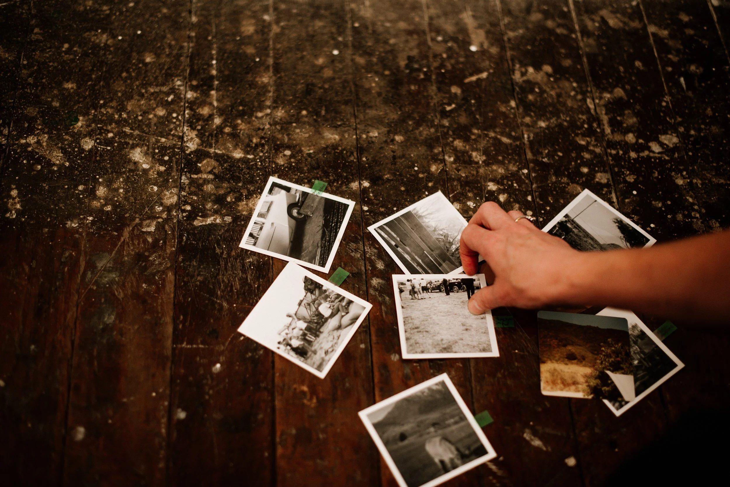 A person's hand holding and sorting black and white photographs on a dark, speckled wooden surface.