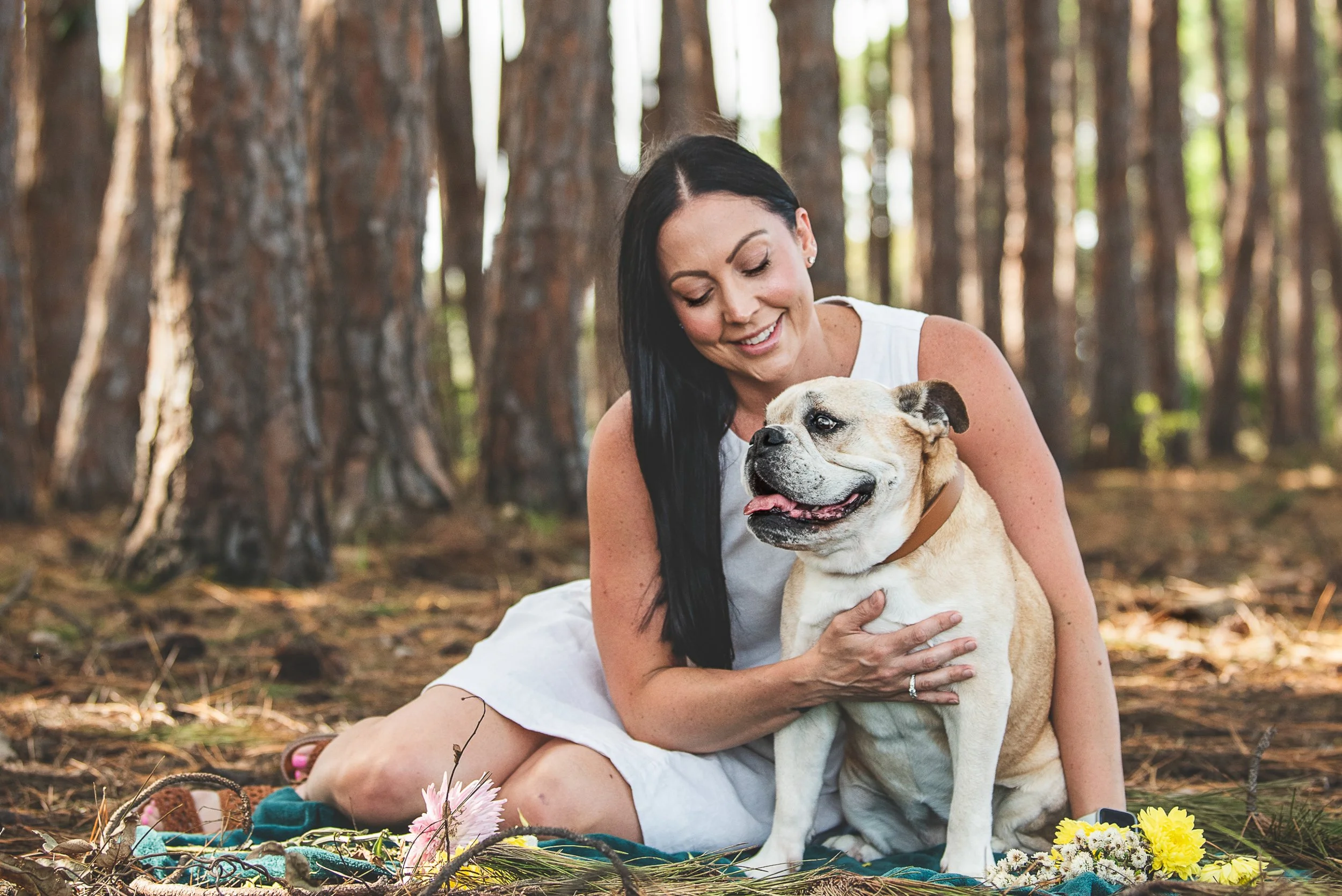 A peaceful portrait of a woman sharing a quiet moment with her British Bulldog among the pine trees. This outdoor pet photography session beautifully captures the love and companionship between owner and dog. PHOTO BY PAWTISTIC MEDIA