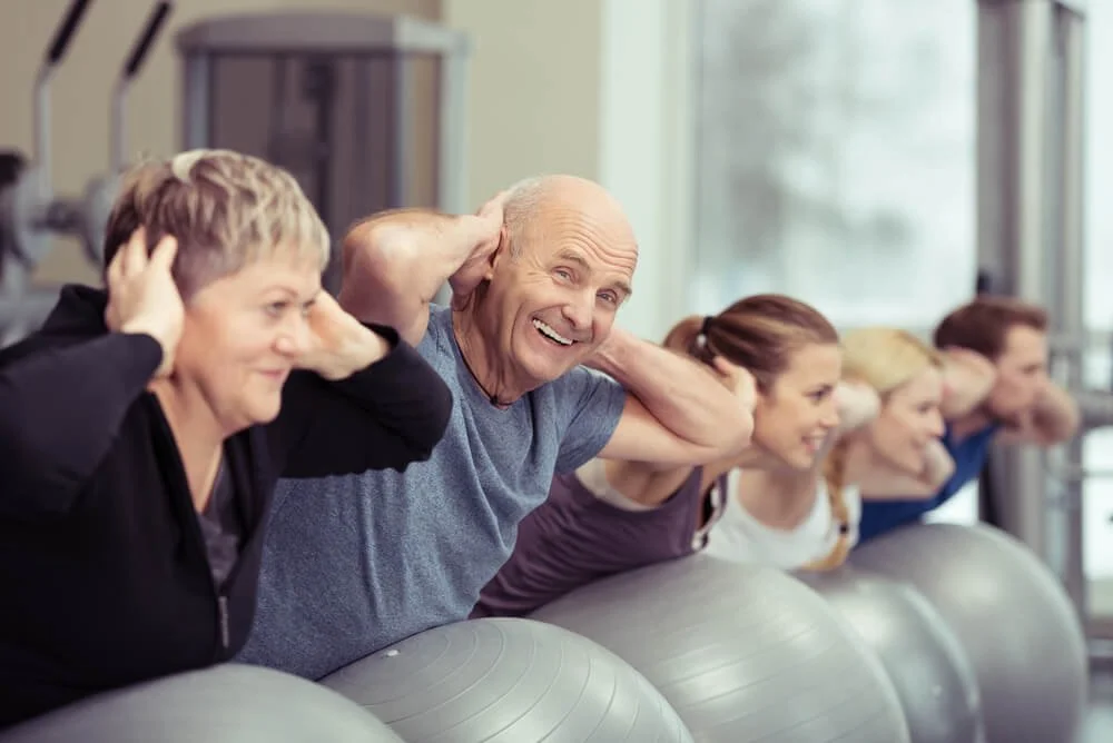 Group of seniors doing seated exercise with fitness balls in a gym