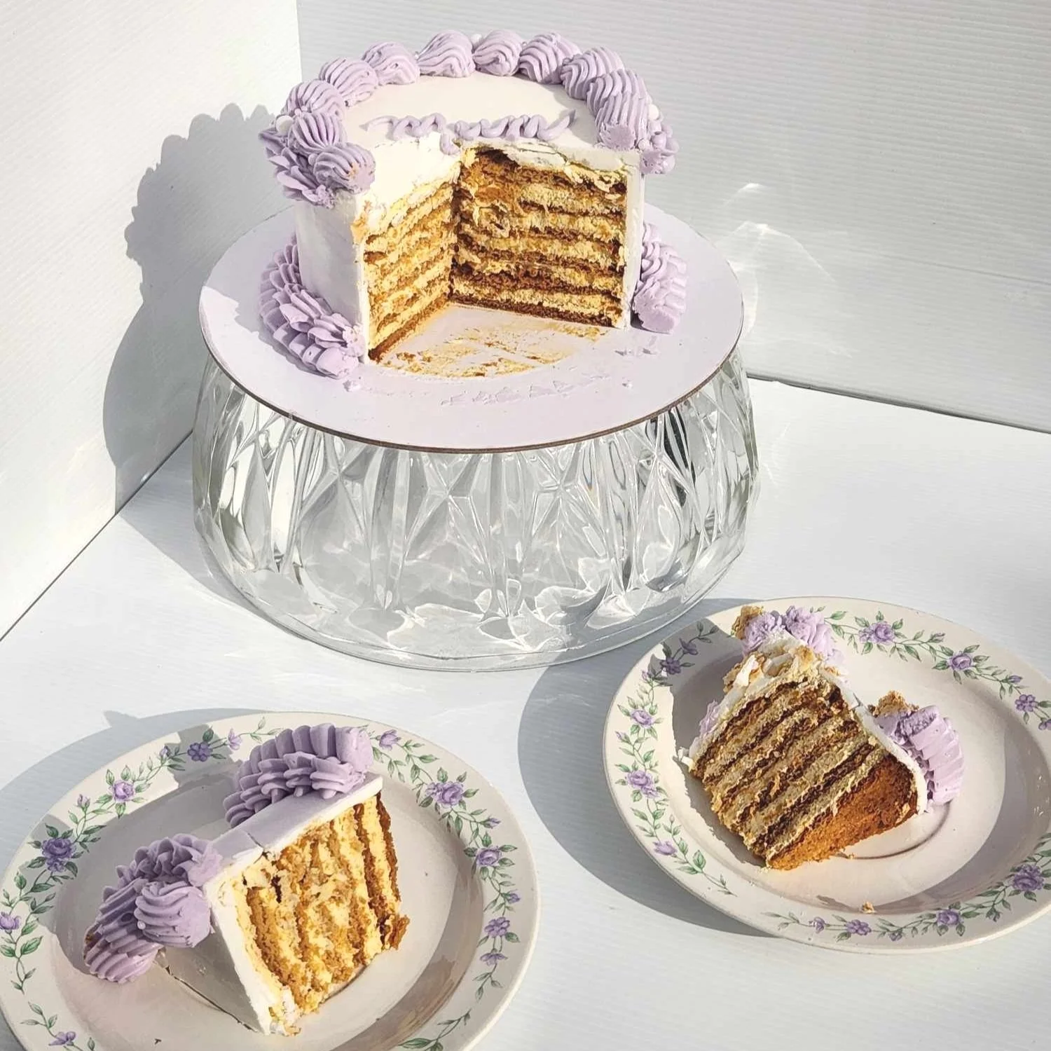 Layered cake with purple frosting on a glass stand, two slices on plates.
