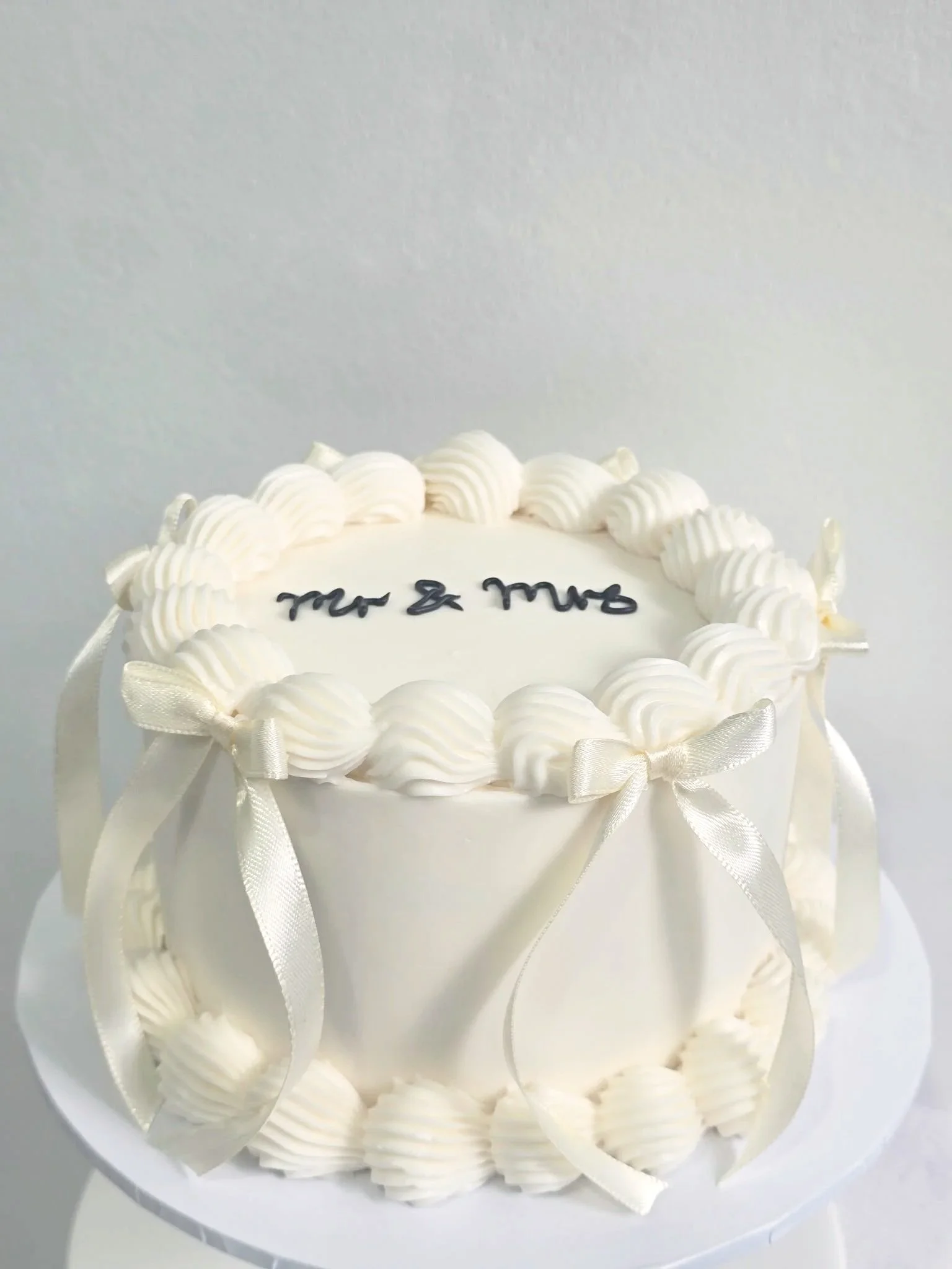 White birthday cake decorated with piped icing rosettes and ribbons, and a message written on top.