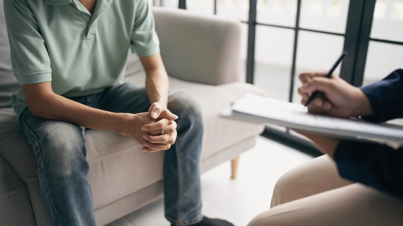 Man sitting on a sofa during a therapy session, talking to a therapist.