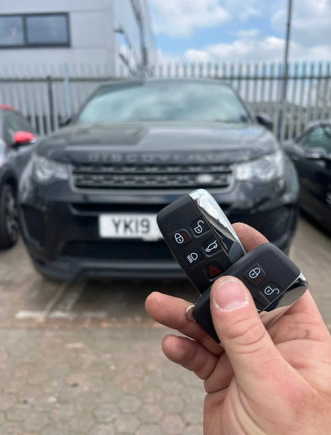 Person holding car keys in front of a black Land Rover Discovery with visible license plate.