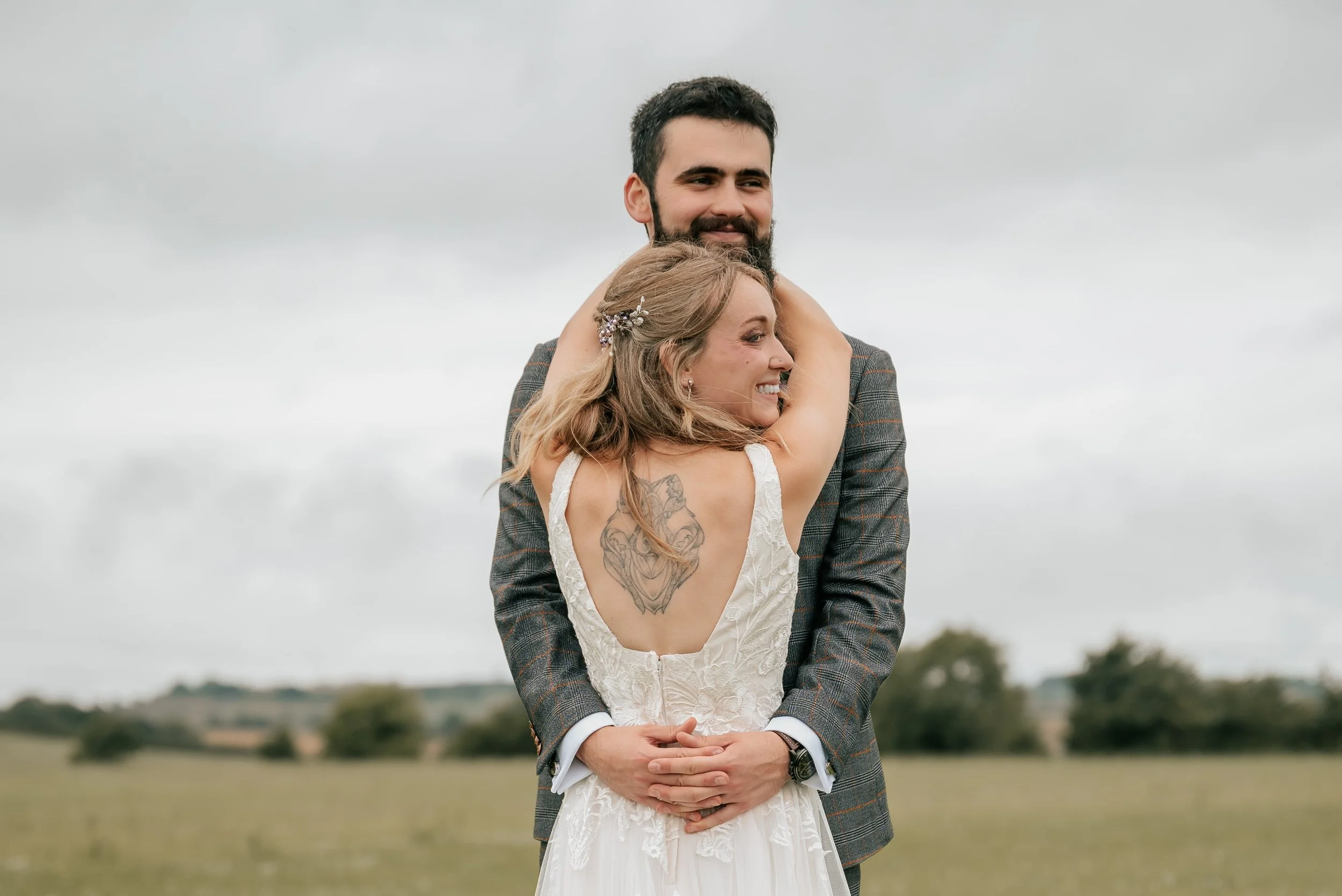 A happy couple hugging outdoors on a cloudy day, with the woman in a wedding dress and the man in a suit.