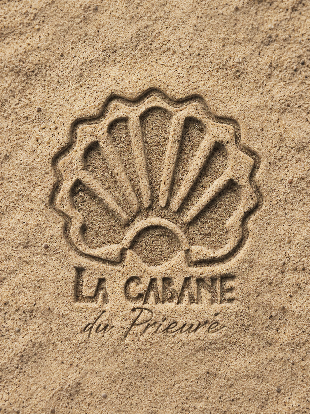 Création assistée IA. Image d’application empreinte sur sable du logo de La Cabane du Prieuré réalisée avec l’aide de la rédaction d’un prompt IA.