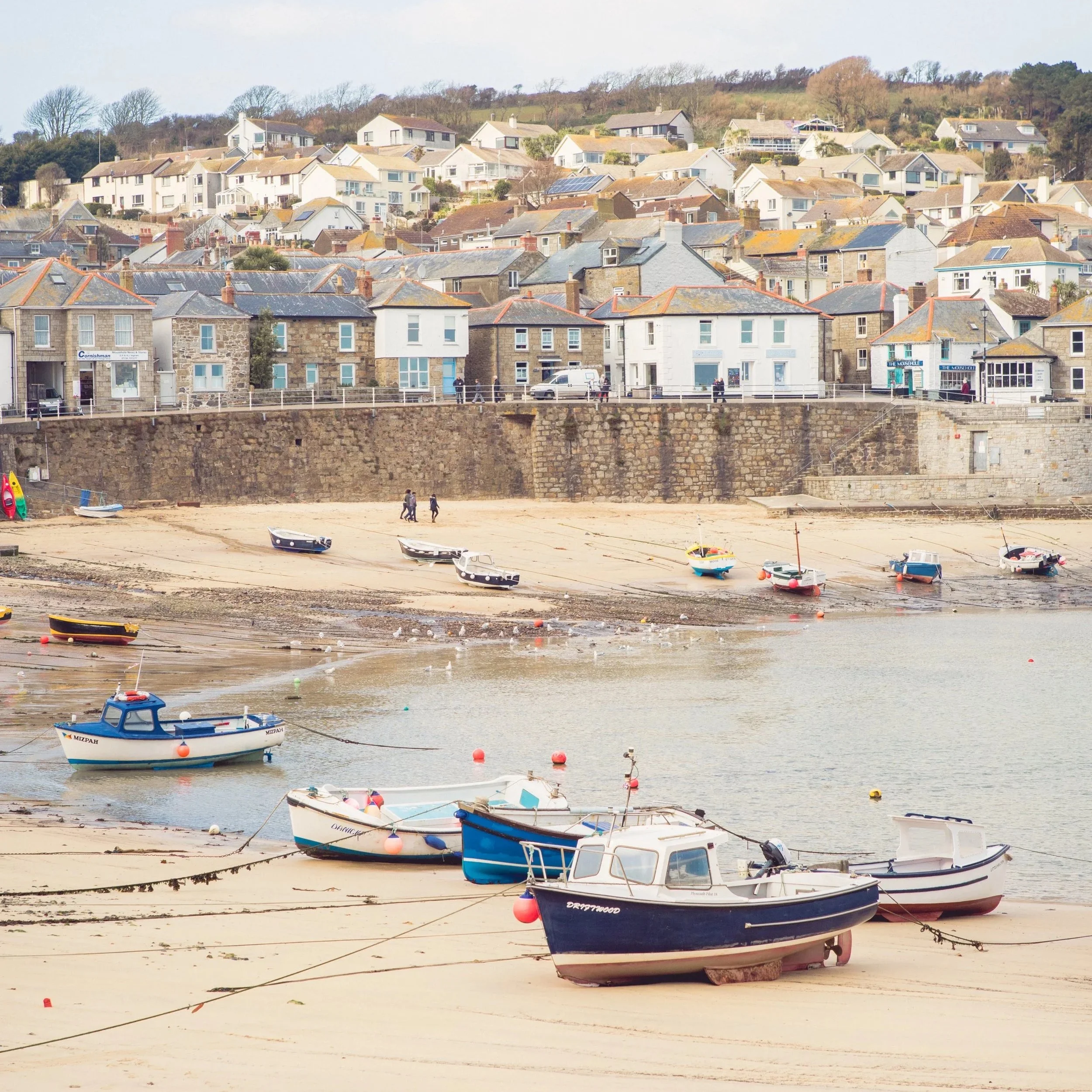 Newlyn harbour in Cornwall, near Artist Residence Penzance, with colourful fishing boats, a sandy beach and traditional seaside houses.