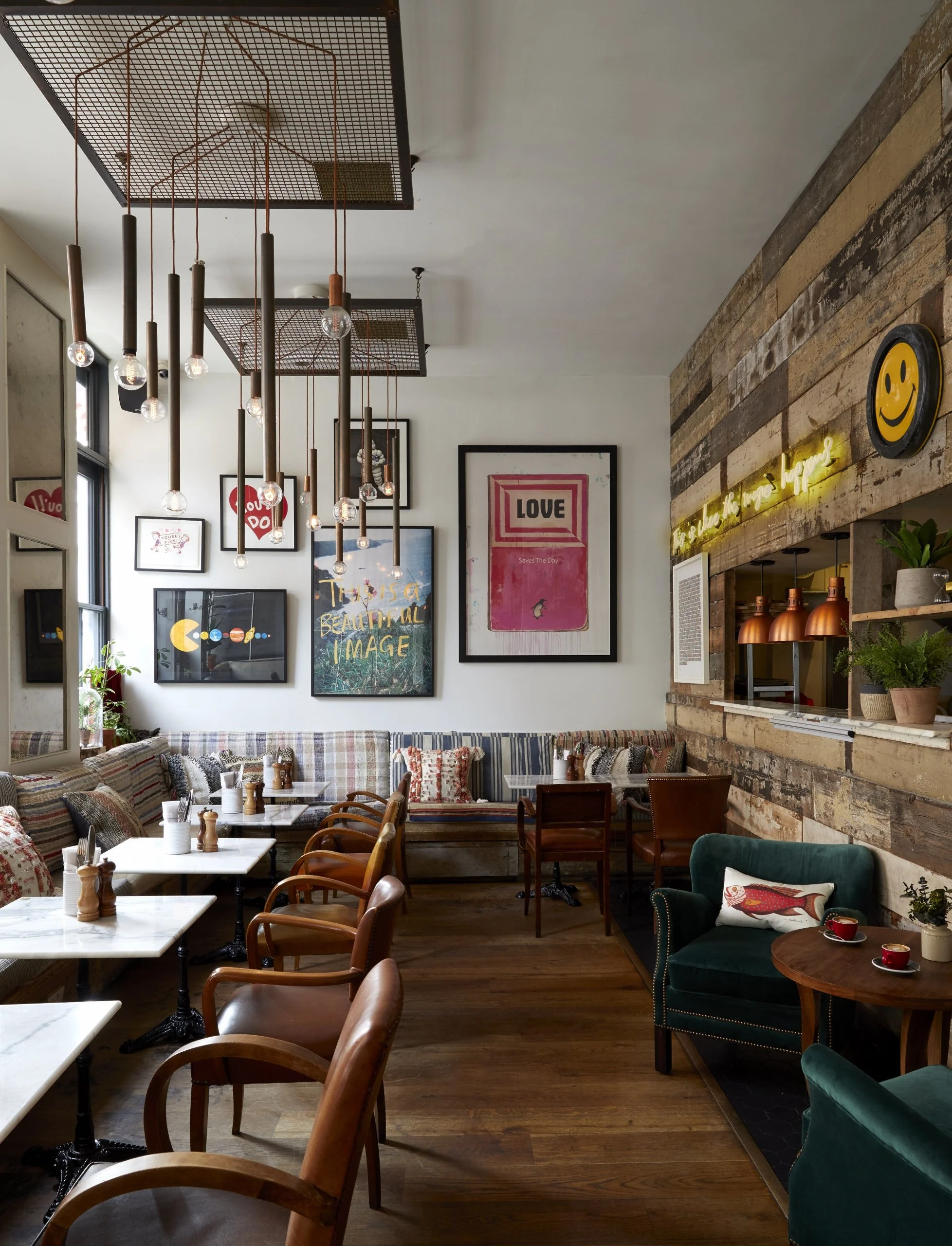 A cozy cafe interior with wooden floors, colorful chairs, marble-topped tables, eclectic wall art, plants, and warm lighting.