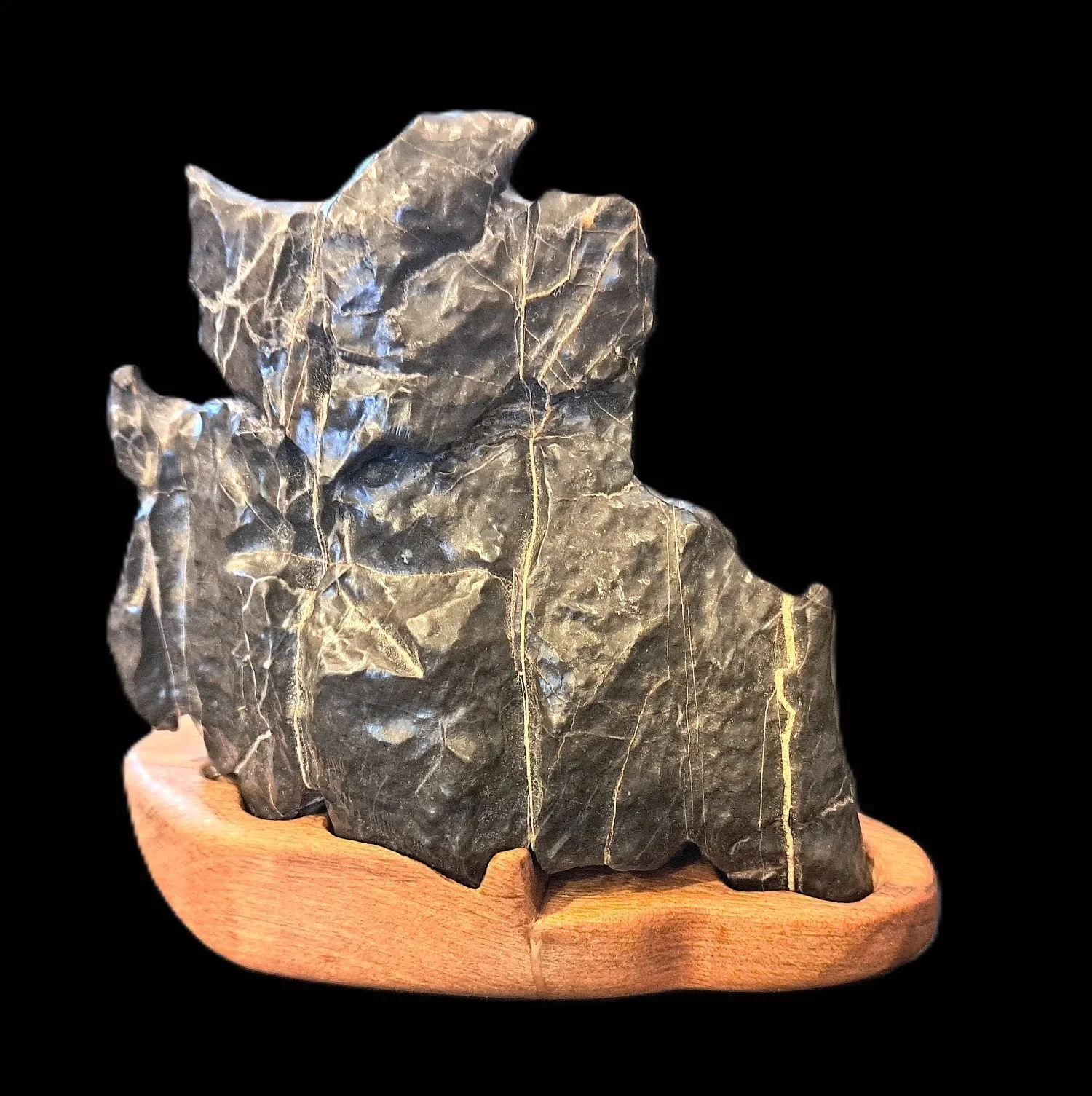 A large, jagged piece of black slate with white veining, mounted on a wooden base against a black background.