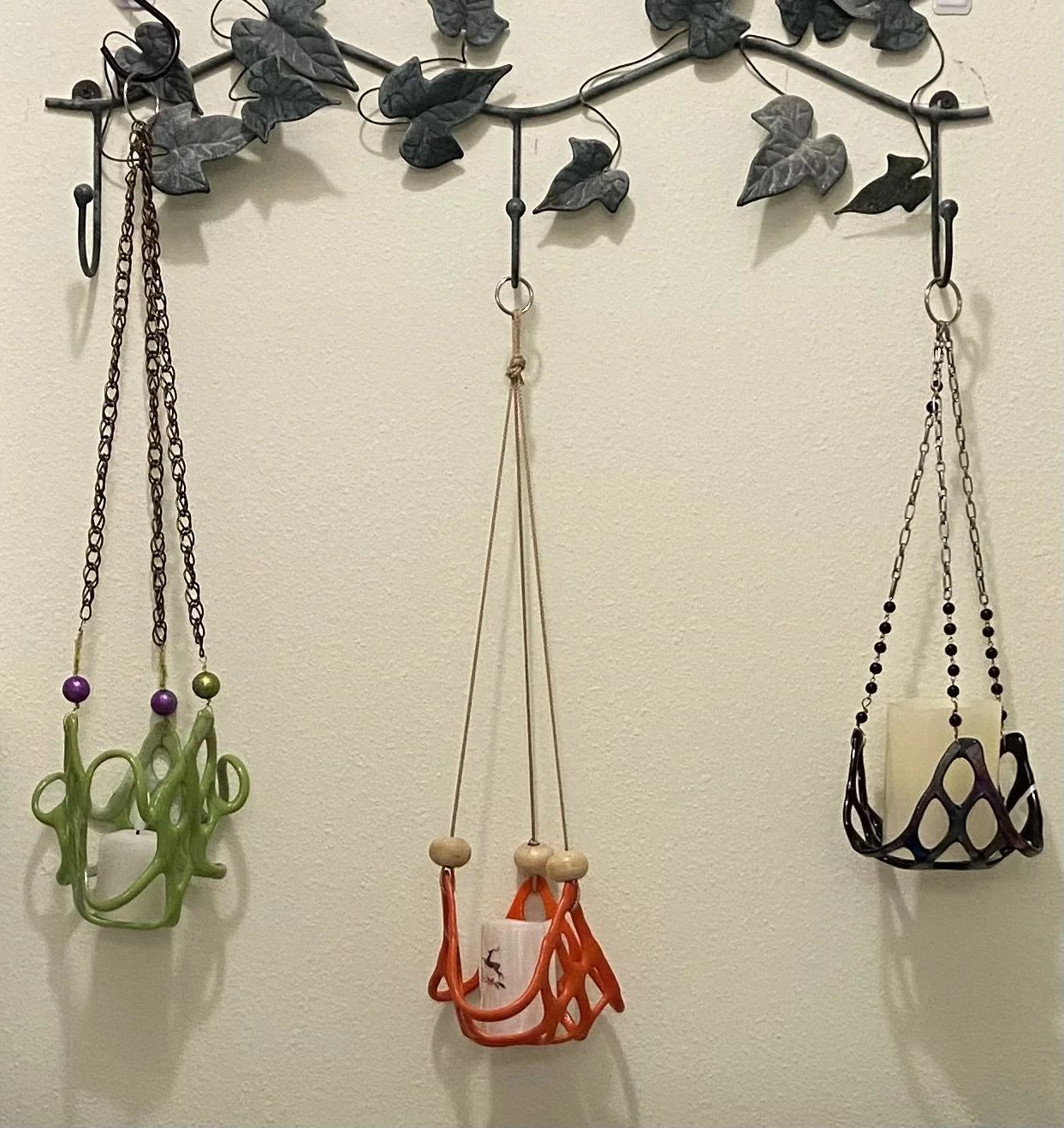 Decorative wall hook rack with ivy leaves, holding three colorful necklaces with pendant charms.