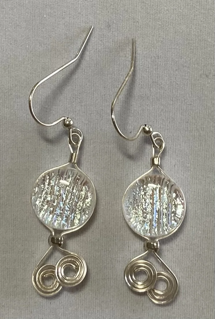 Silver earrings with a circular, textured design and spiral accents at the bottom.