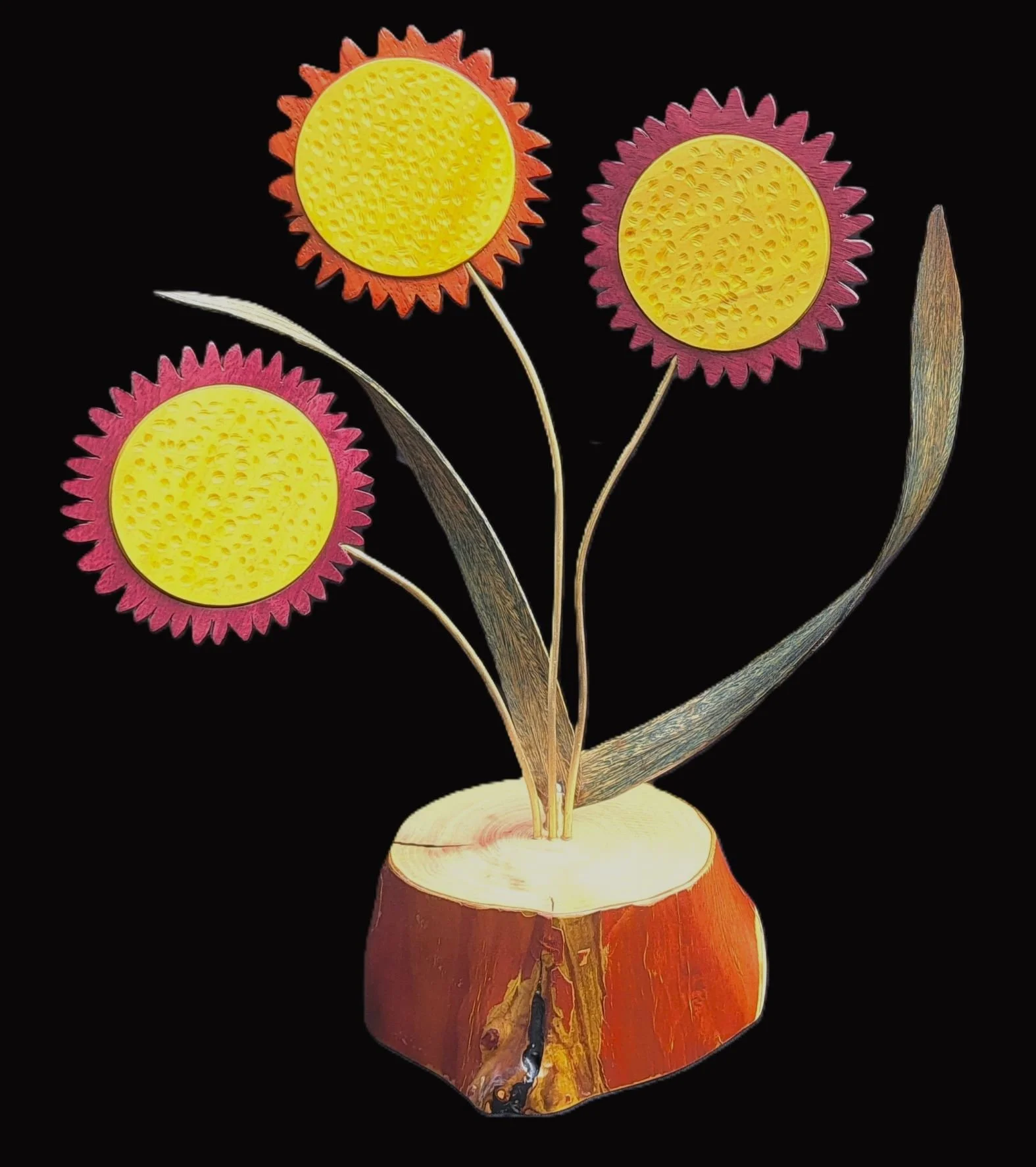 Wooden flower sculpture with three yellow and pink vibrant flowers and two silver leaves, set against a black background.