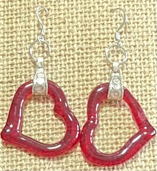 Pair of red heart-shaped acrylic dangle earrings with metal hooks on burlap background.