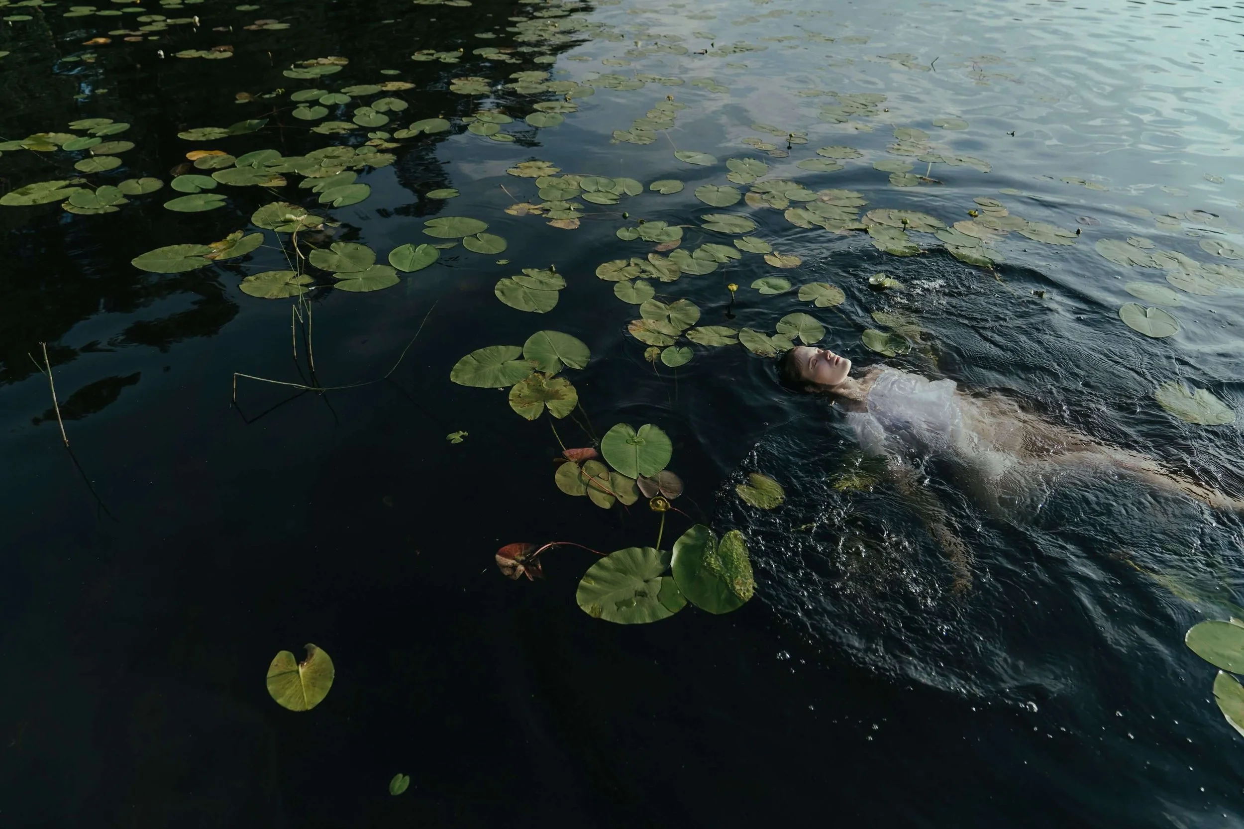 A person swimming in a pond or lake with lily pads floating on the water.