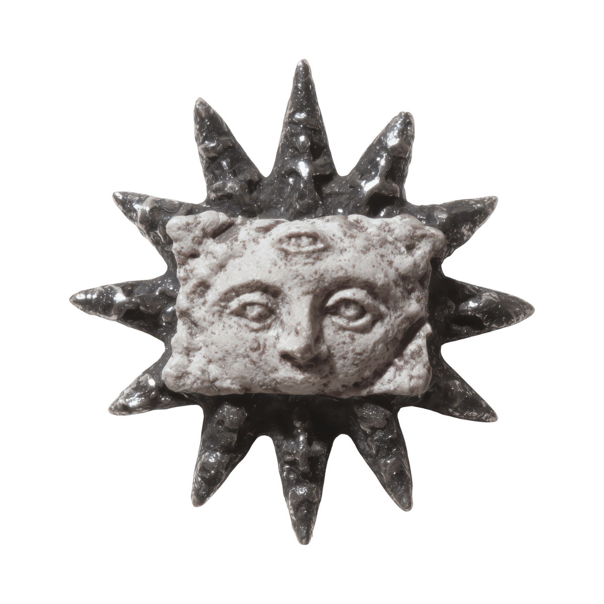 A sculpture of the sun with a human face, a third eye on the forehead, and sun rays extending outward, made of textured stone or metal.