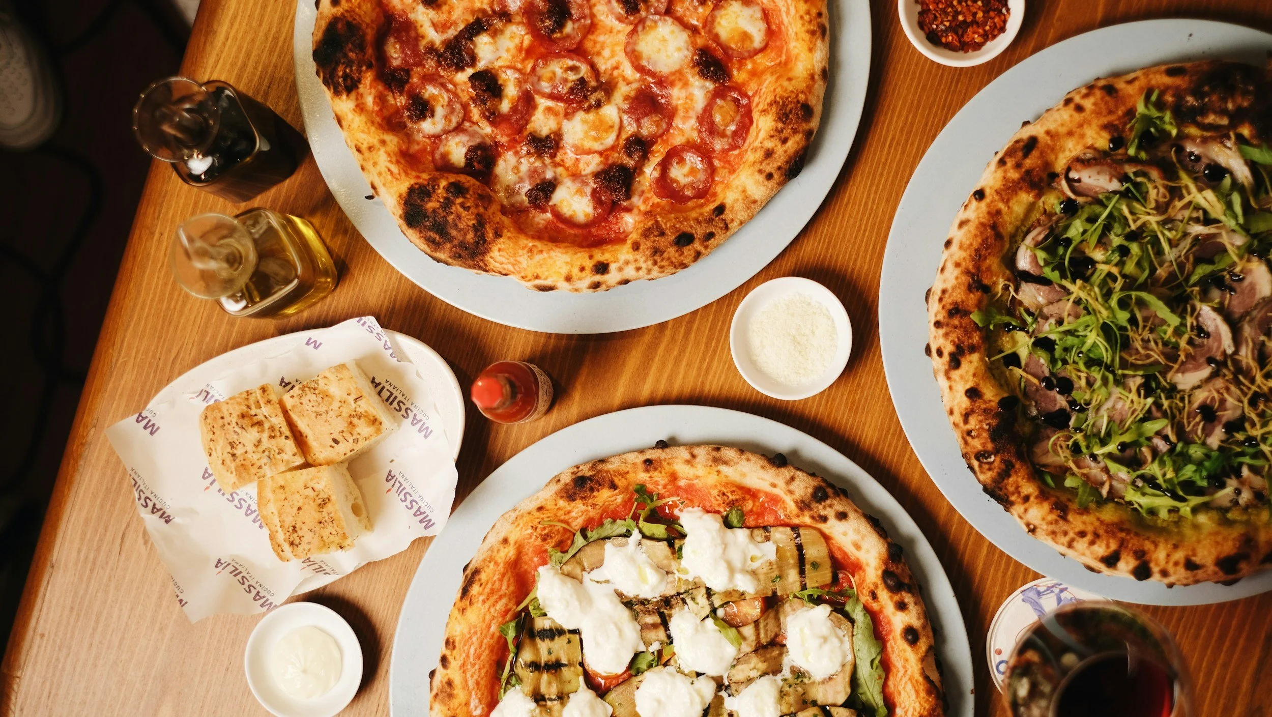 Person holding a smartphone with a text message on the screen, with a laptop and a stack of hundred-dollar bills on a white desk.