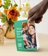 A hand holding a feedback survey card next to a vase of flowers on a table.