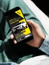 Person holding a smartphone displaying an advertisement for a car dealership offering $5800 off on select new cars, with a picture of a white SUV and options to claim the offer or save it for later.