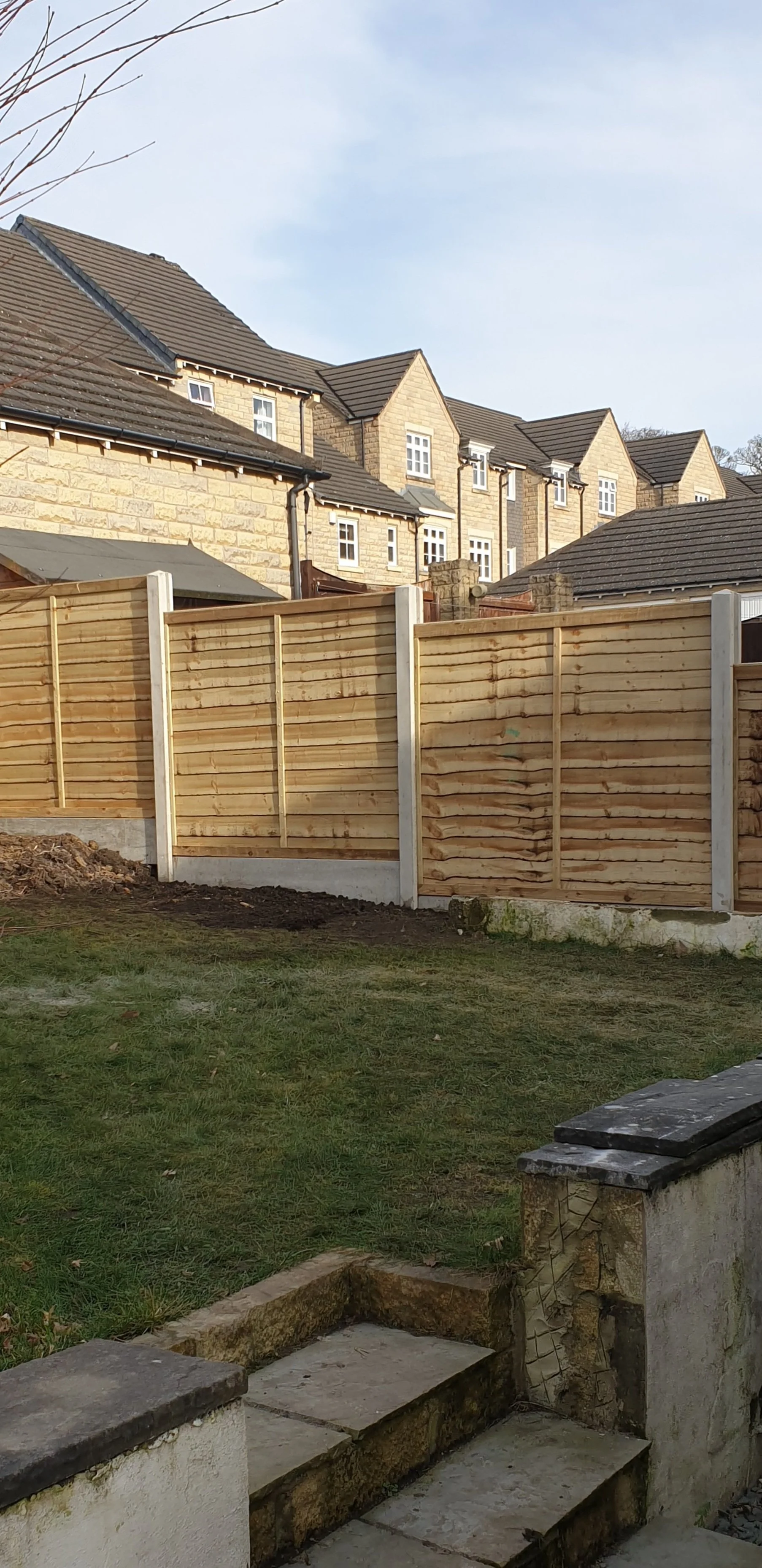 Backyard view with wooden fence, brick houses, and steps leading to grassy area.