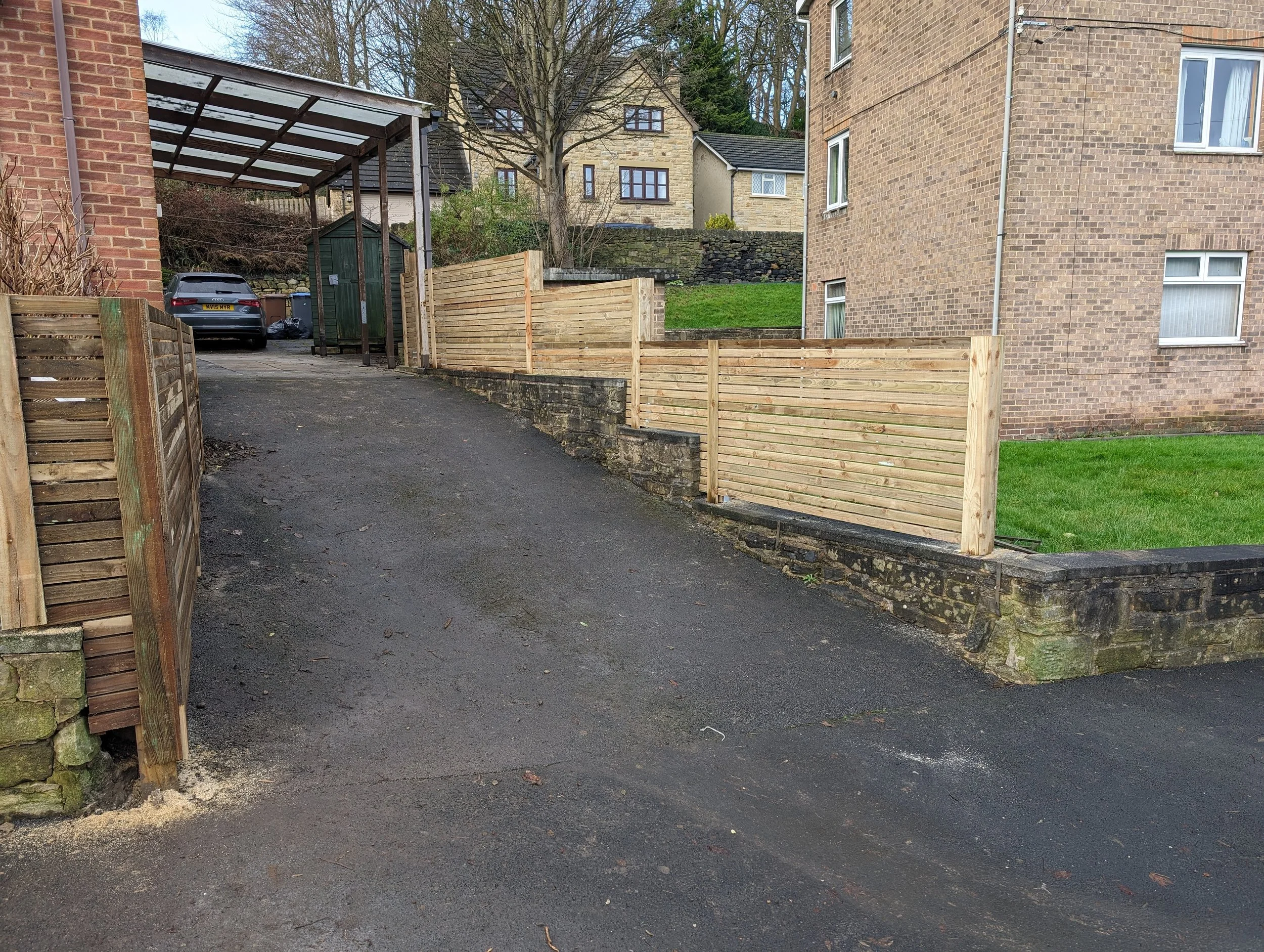 Driveway with wooden fencing, car-port, parked car, and residential buildings