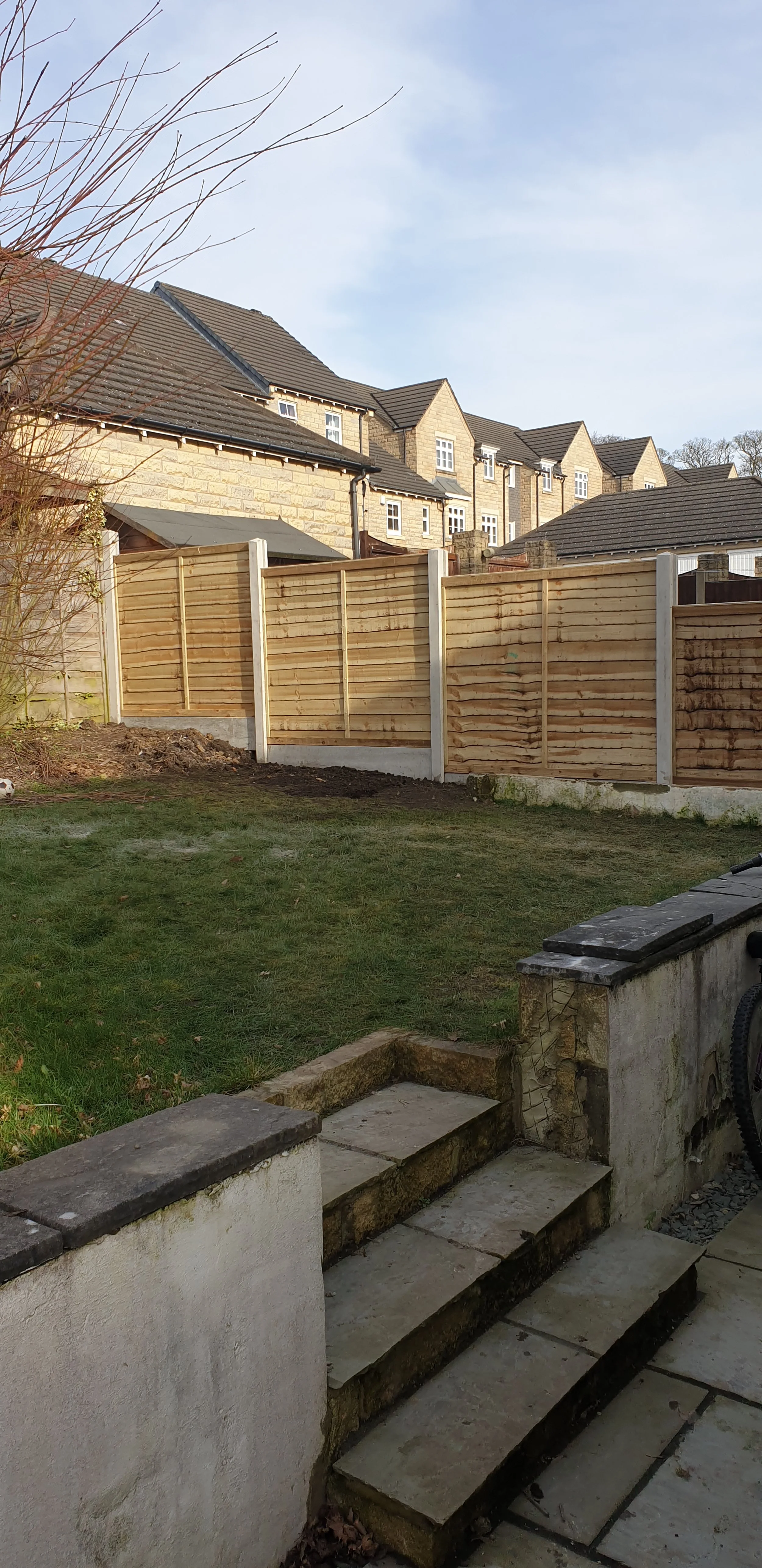 Backyard with stone steps, grass, wooden fence, and brick houses.