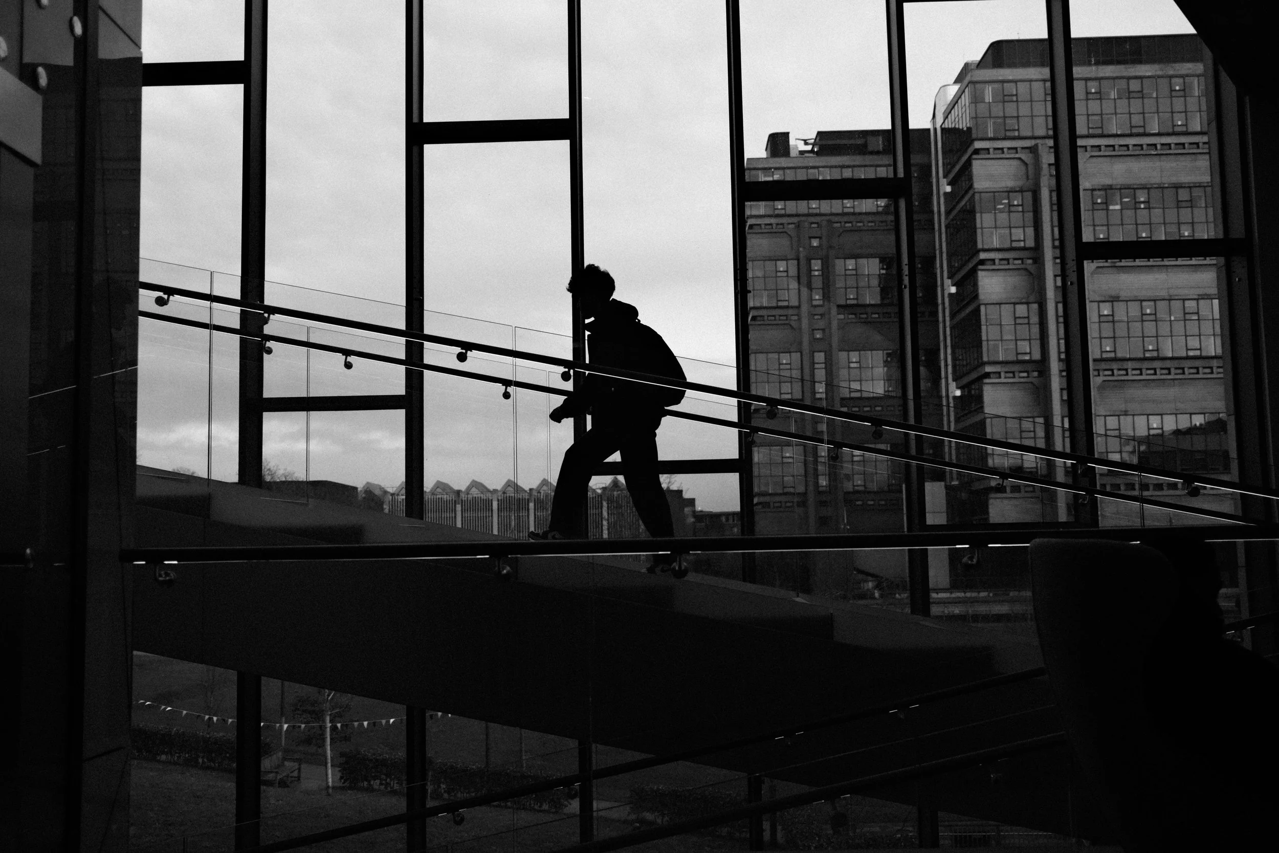 A student's silhouette climbing a glass staircase at the end of a school day, in black and white