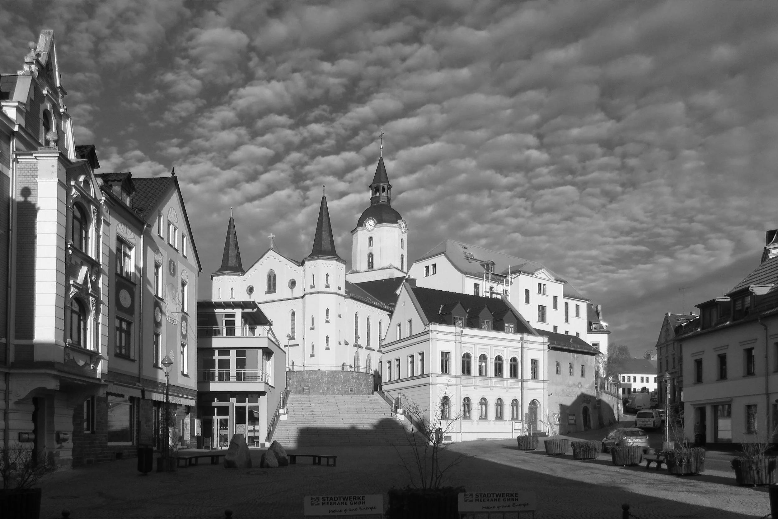 Empty town square and church steps under a patterned cloudy sky, evoking the marketplace of the laborers.
