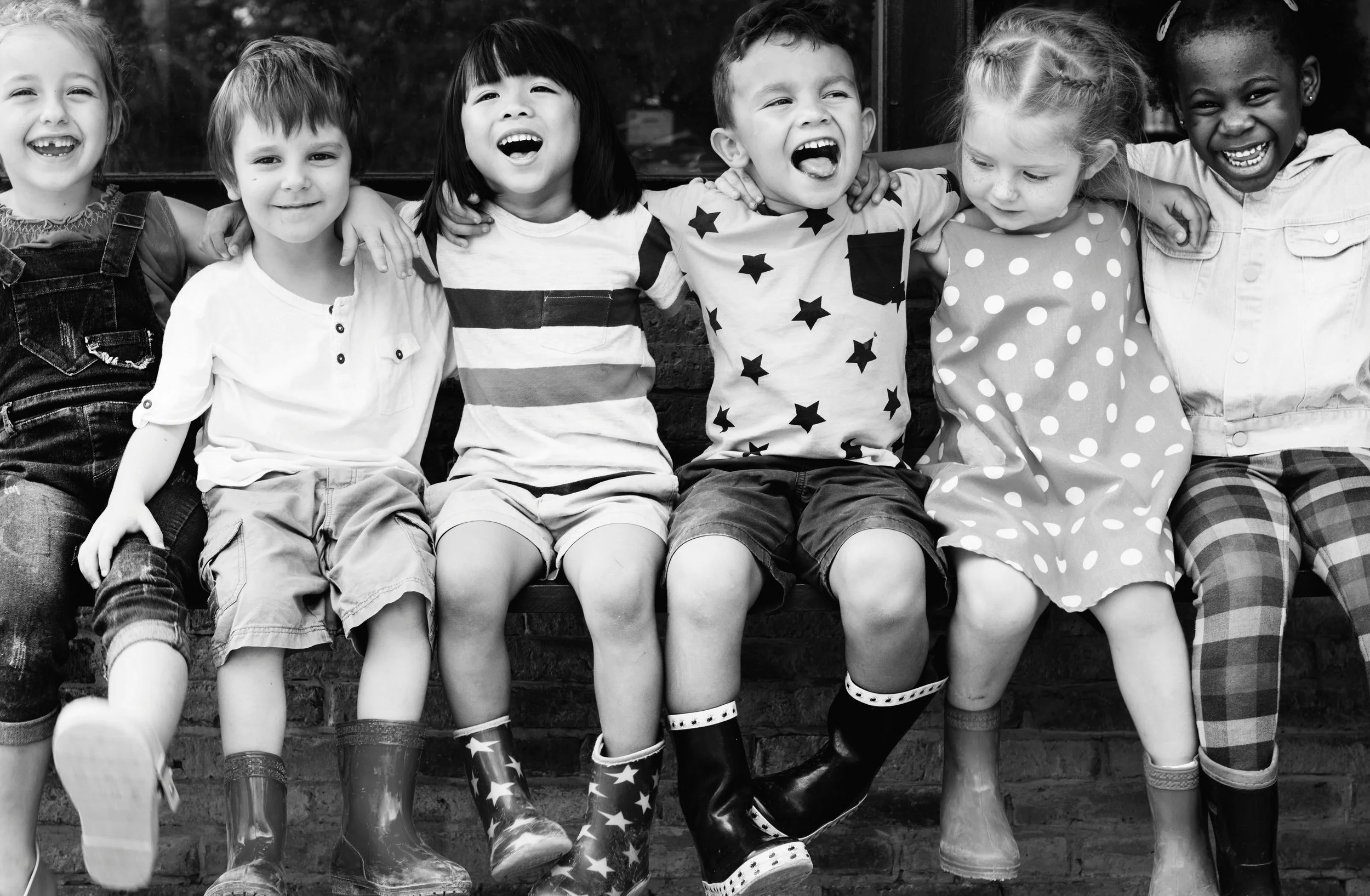 Group of children sitting together with their arms around one another, smiling and sharing a moment of friendship.