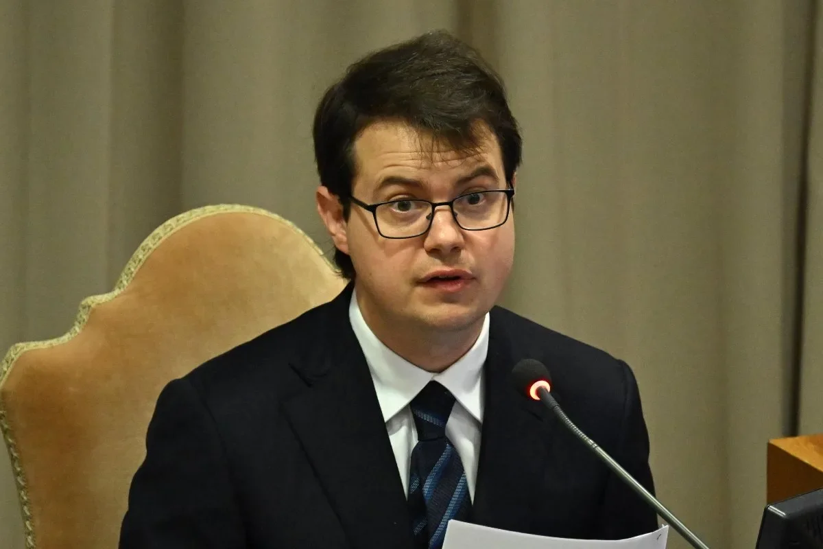 AI researcher Chris Olah speaking into a microphone while wearing a suit and tie at an official presentation.