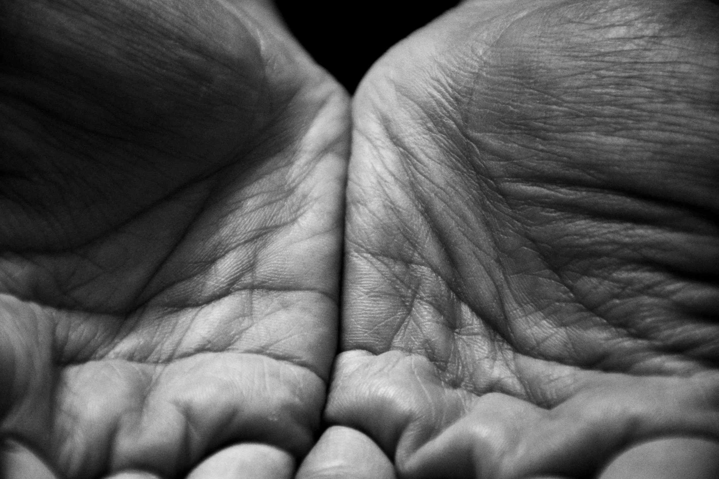 Black-and-white close-up of two open, weathered palms cupped together in vulnerability and receptivity.
