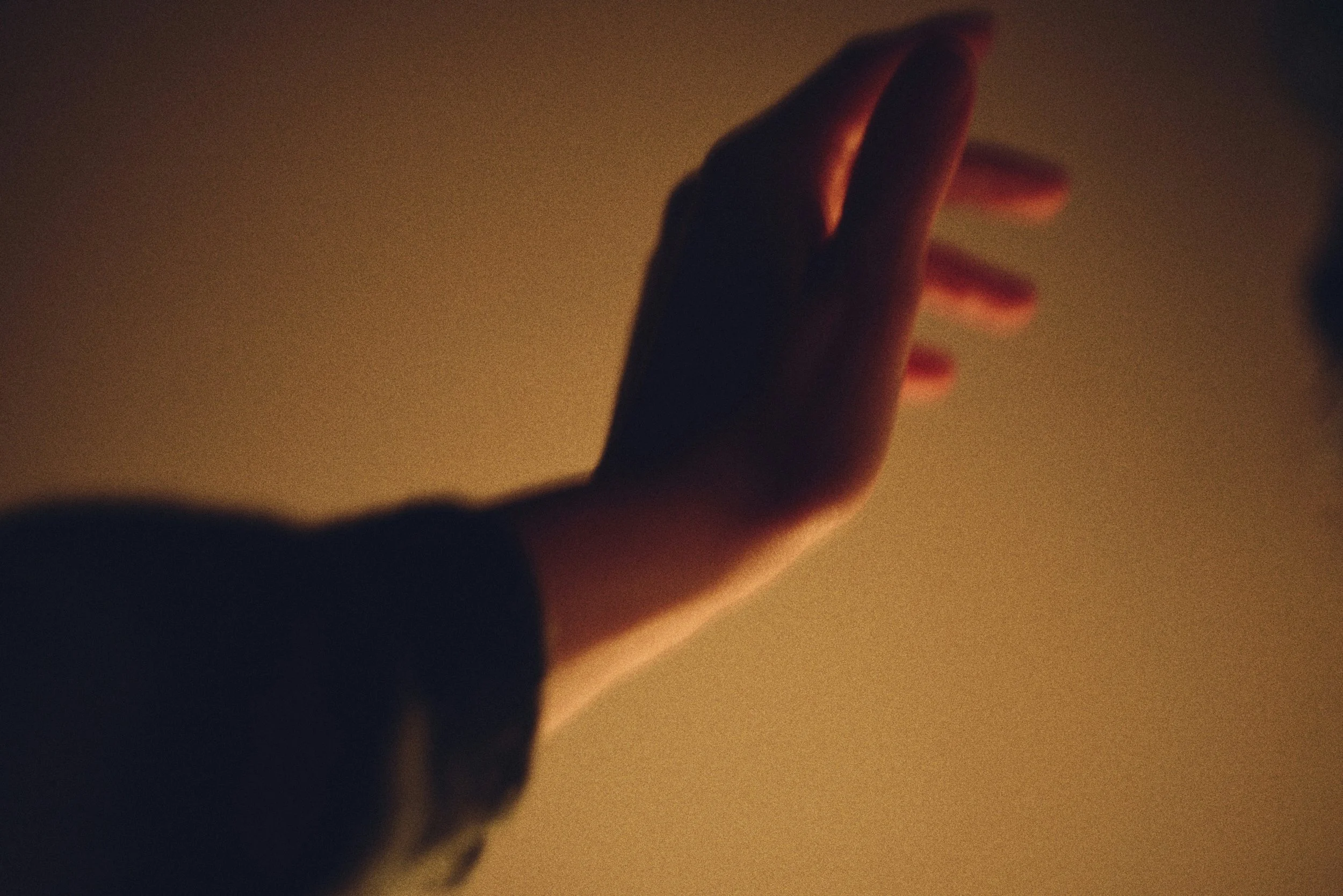 A single open hand reaching upward toward warm golden light in the darkness
