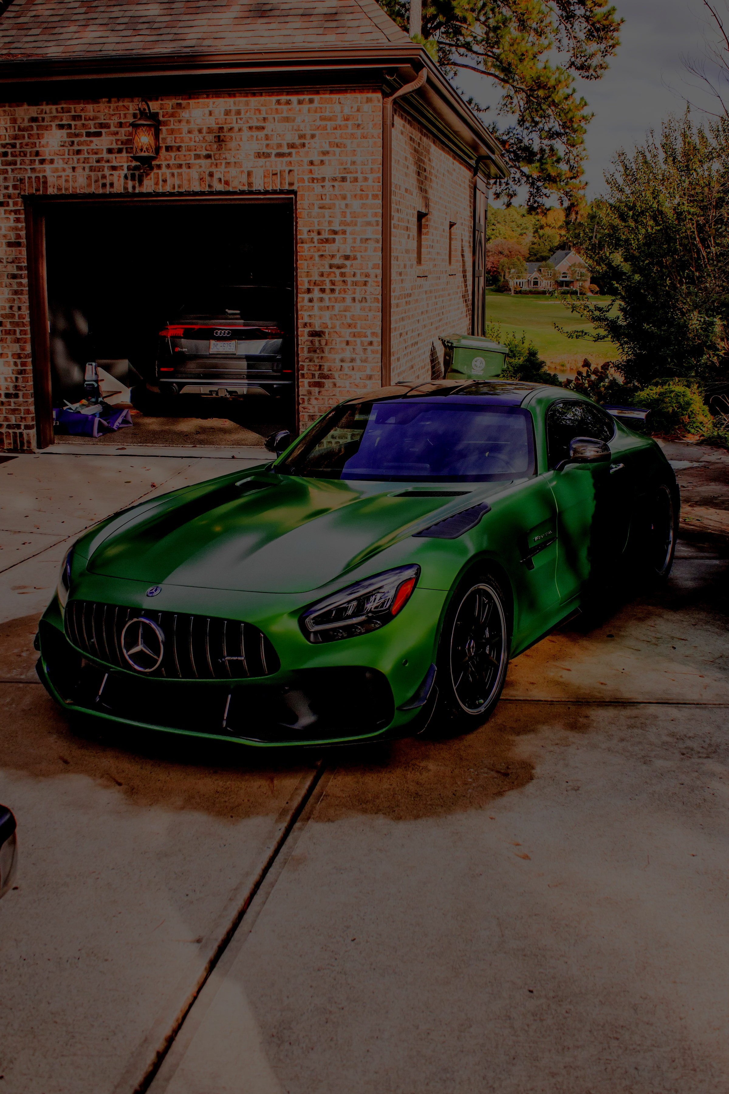 Young man with sunglasses and black long sleeve shirt giving a thumbs-up while holding a scooter in front of a white SUV parked outside a garage.