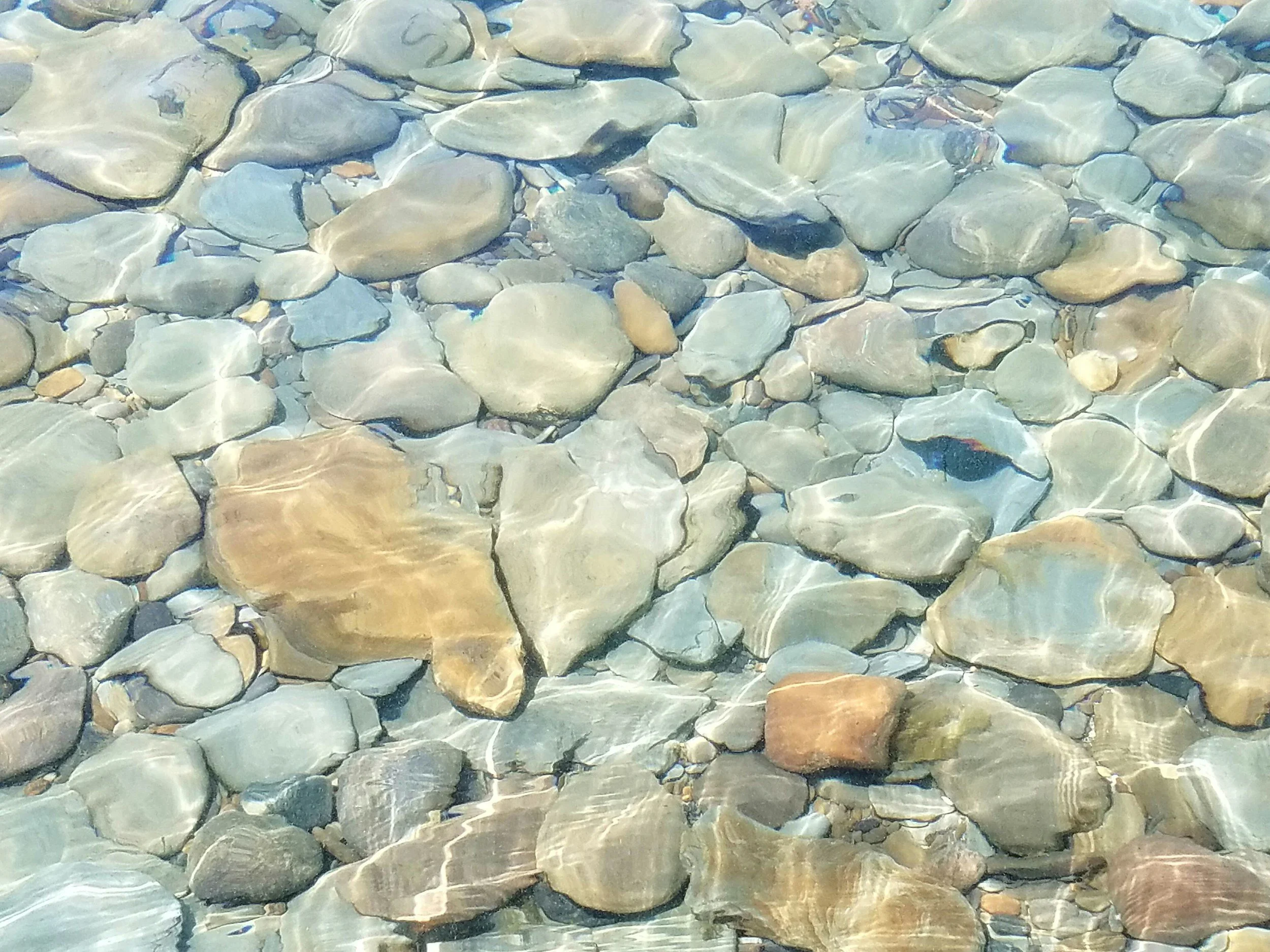 Grey stones under water reflecting light. Grief therapist Longmont, CO. Trauma therapist Longmont, CO