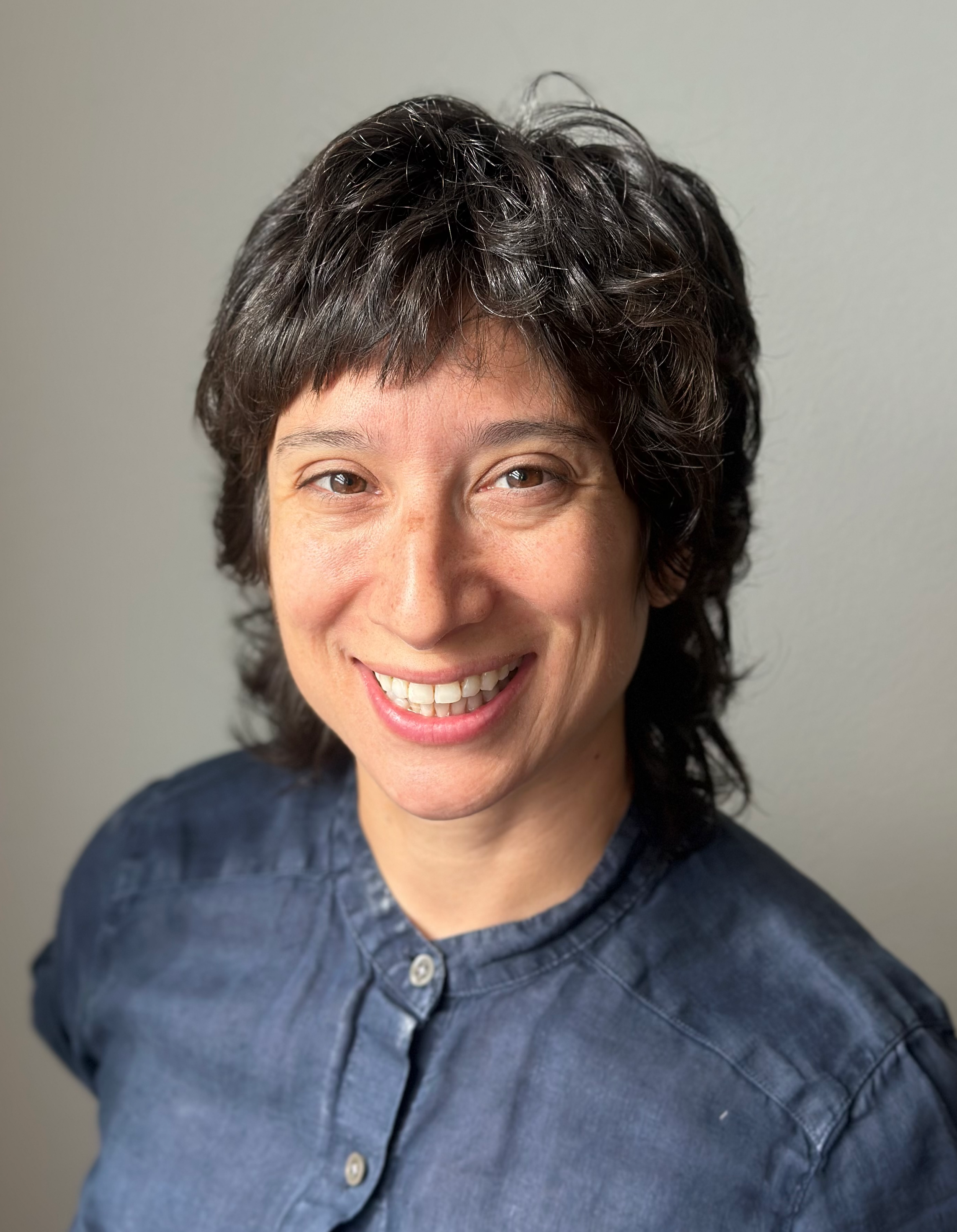 Headshot of Sophia smiling in navy blue shirt, olive skin, dark brown hair with white background. Grief counseling Longmont, CO.