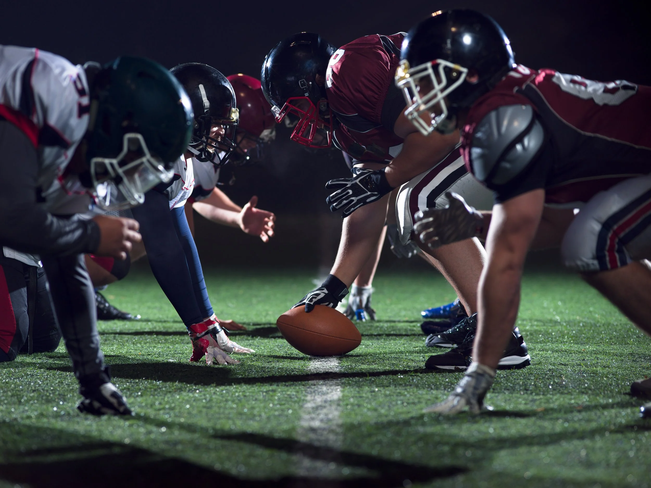 Football players lined up at the line of scrimmage during a night game, ready to start a play.