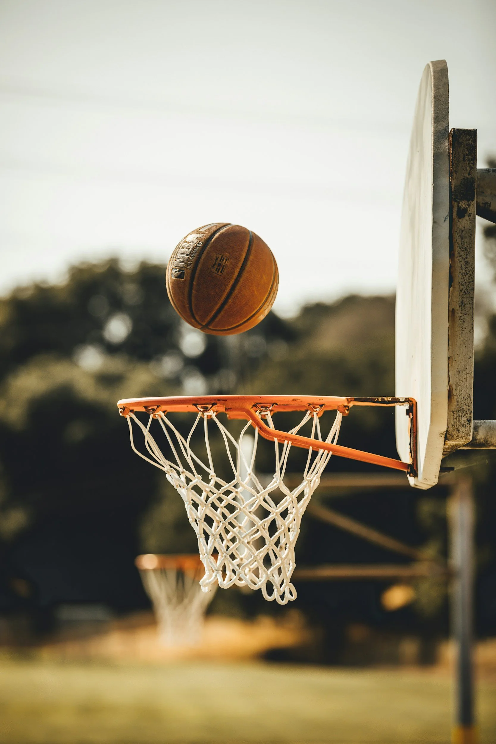 A basketball going through a hoop on an outdoor basketball court.