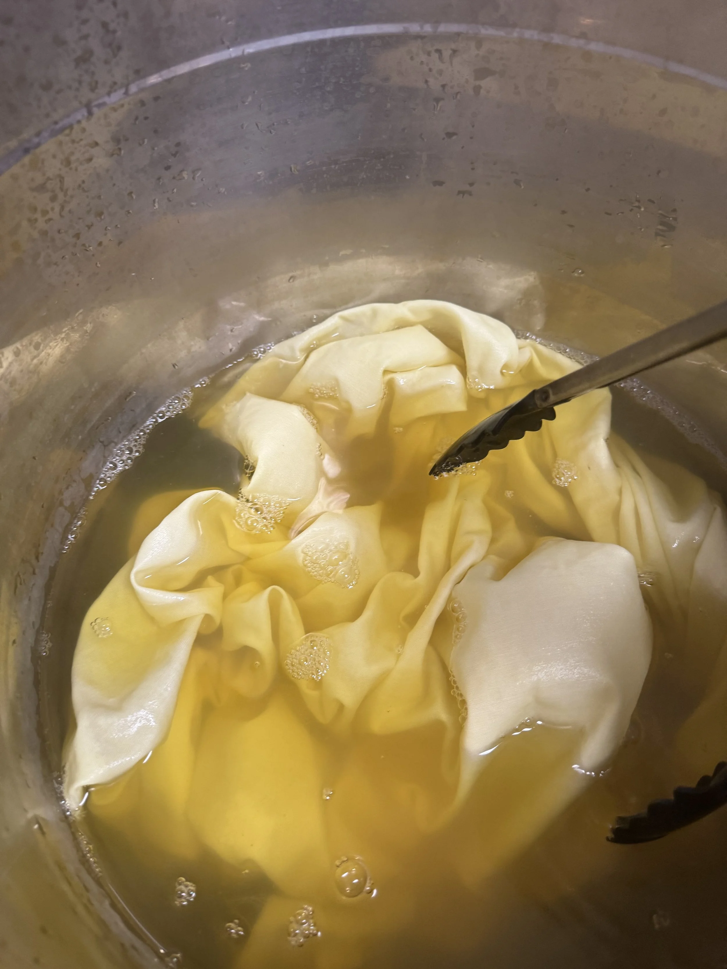 A pot with boiling water and a cheesecloth bag inside, likely for making cheese or cheese-based dish.