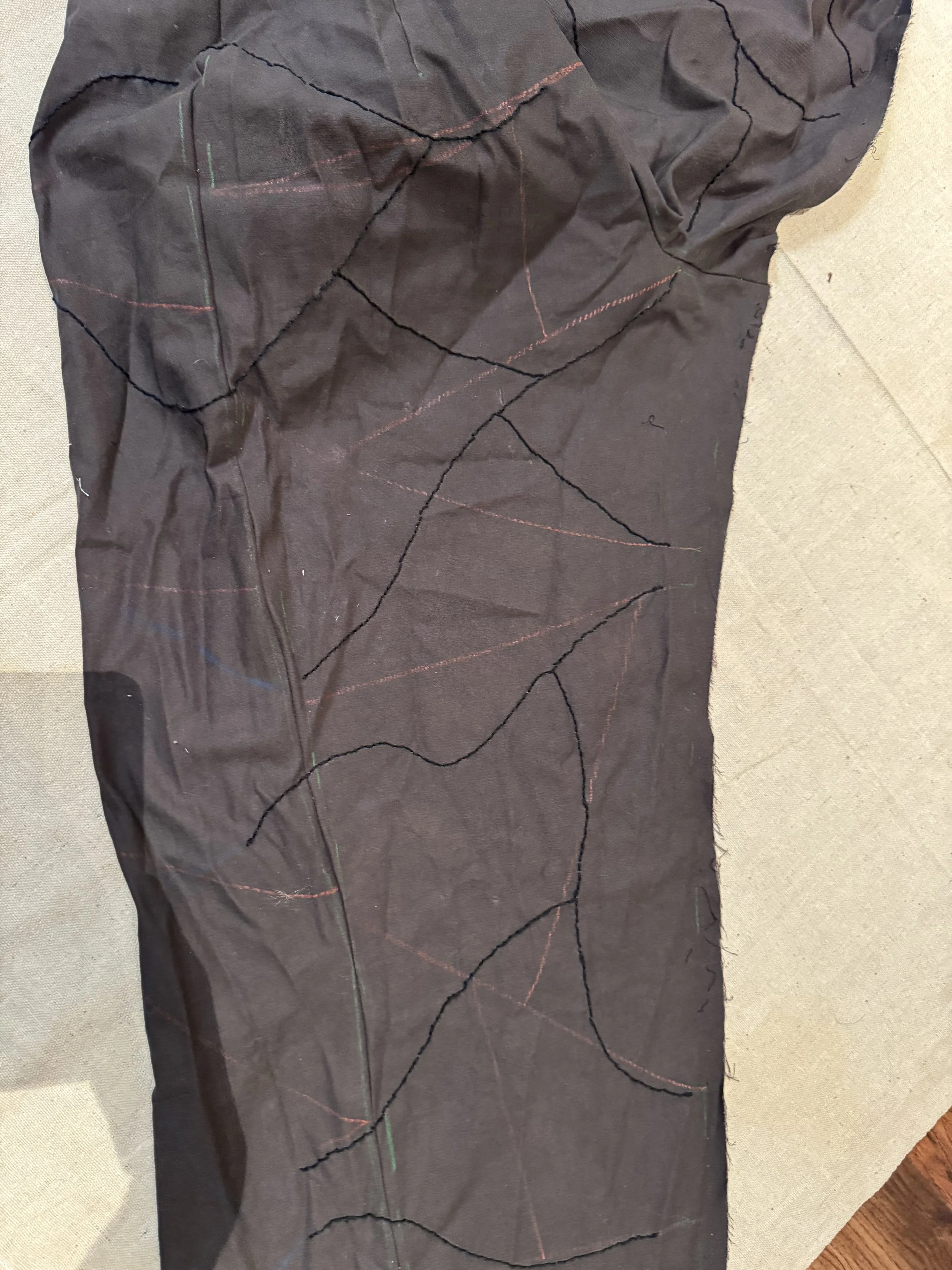 A piece of black fabric with colorful chalk lines drawn in a random pattern, placed on a beige surface.