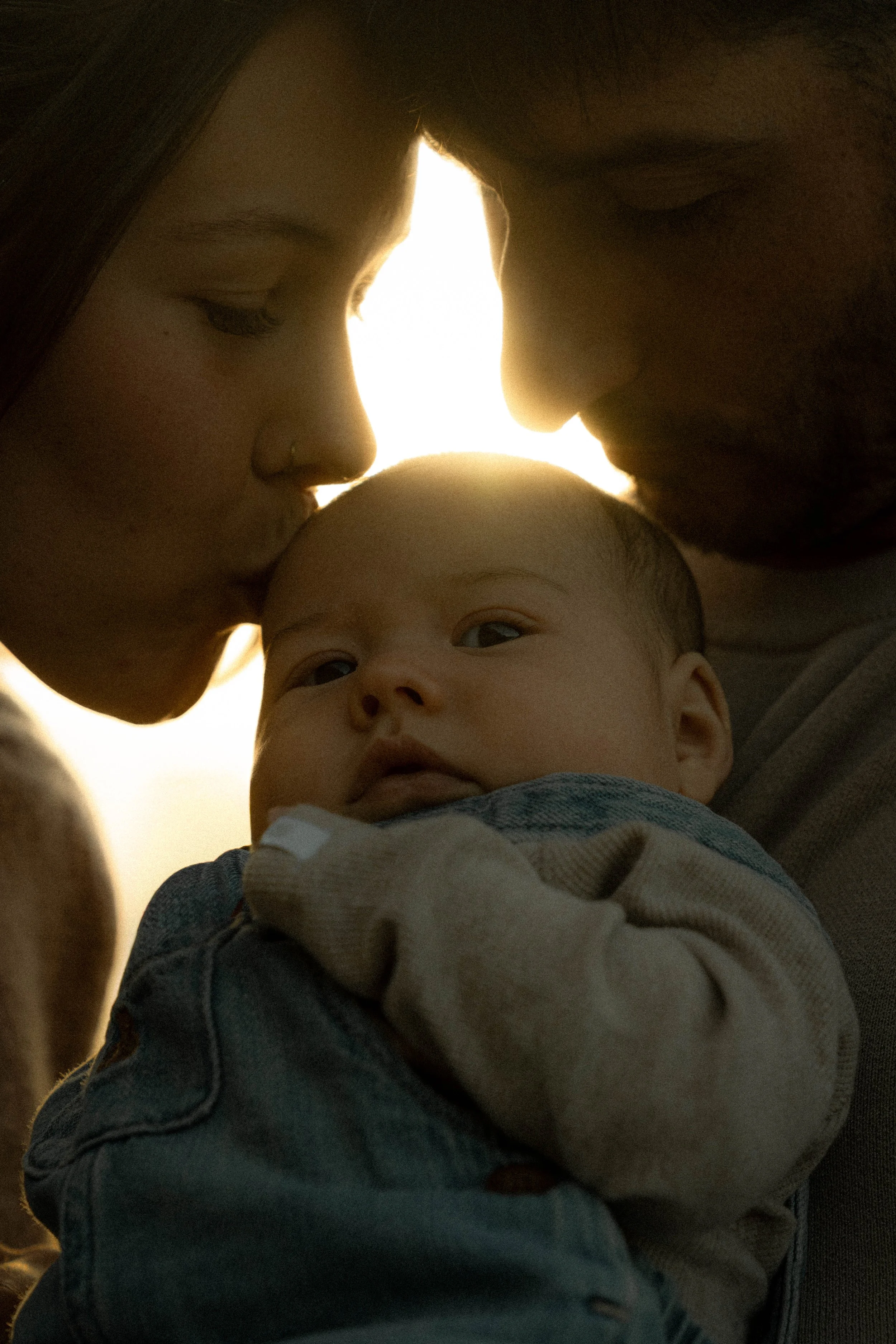 Un adulte et un bébé se touchent le front en face lors d'un moment tendre, avec une lumière douce en arrière-plan.