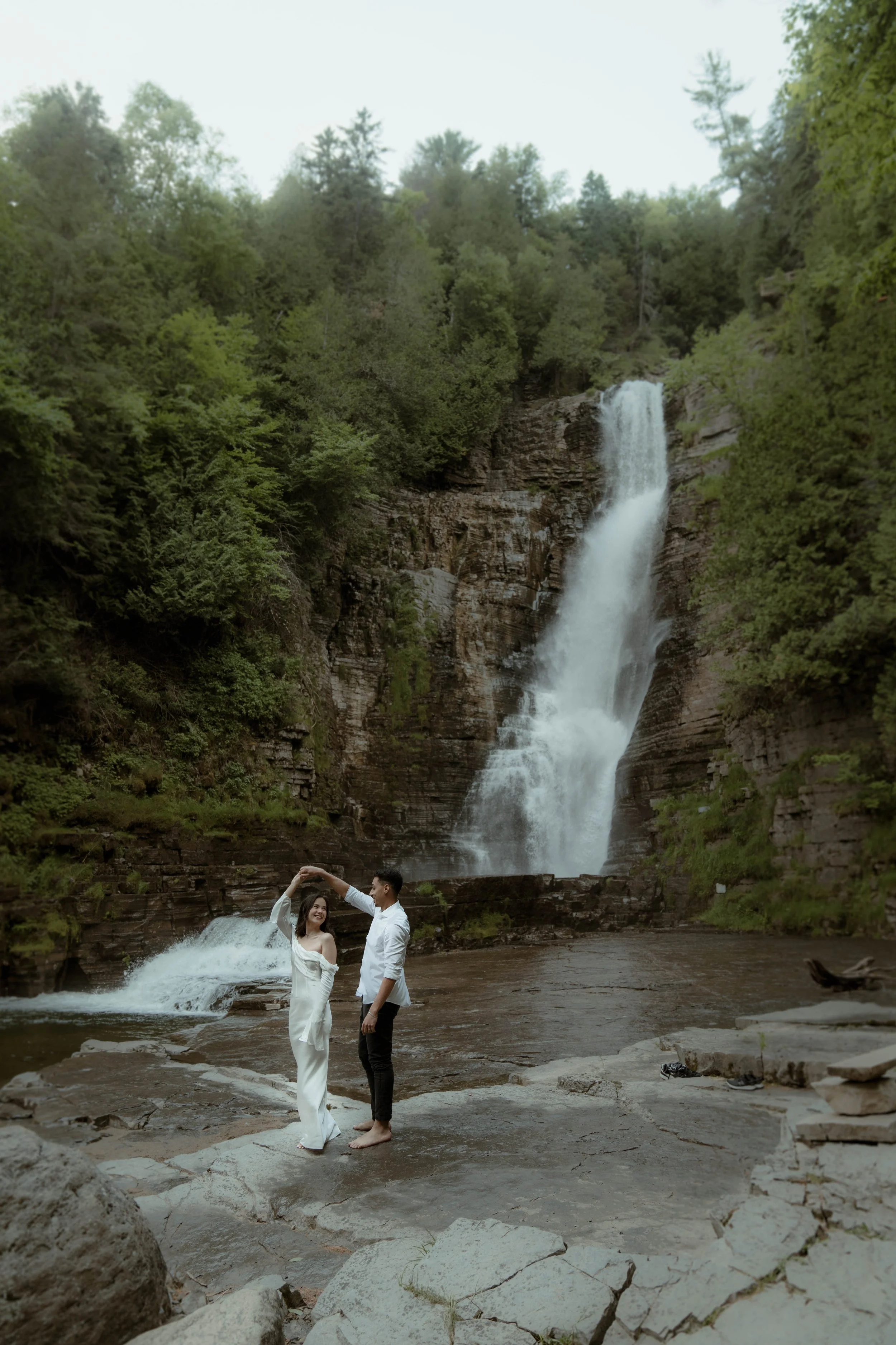 Un couple dansant près d'une cascade entourée d'arbres et de rochers.