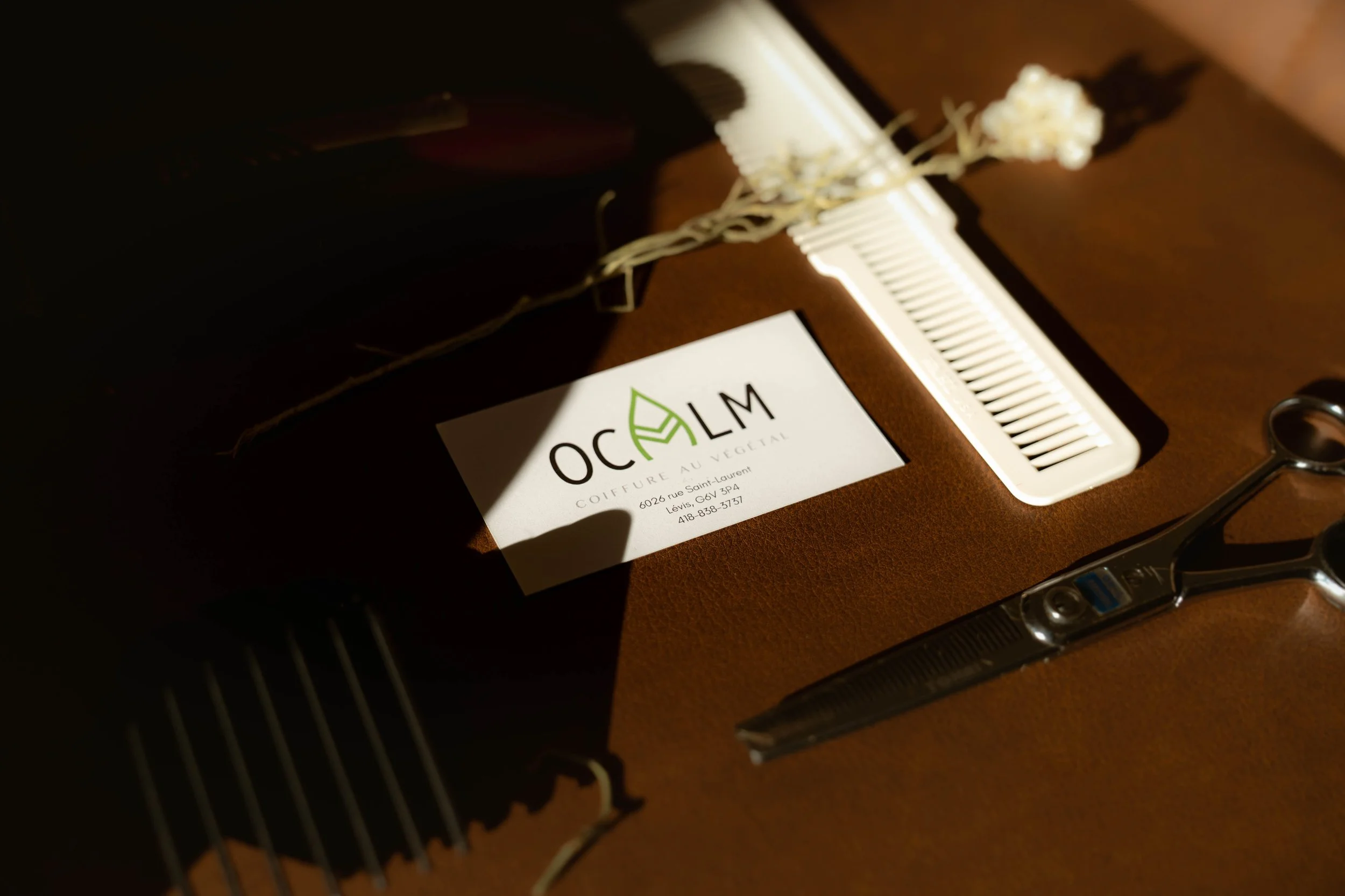 Une table en bois avec une bouteille, une pince à cheveux, une paire de ciseaux, un pinceau, une feuille avec un logo 'OCLM' et un texte en français, et un plastique pour mèches