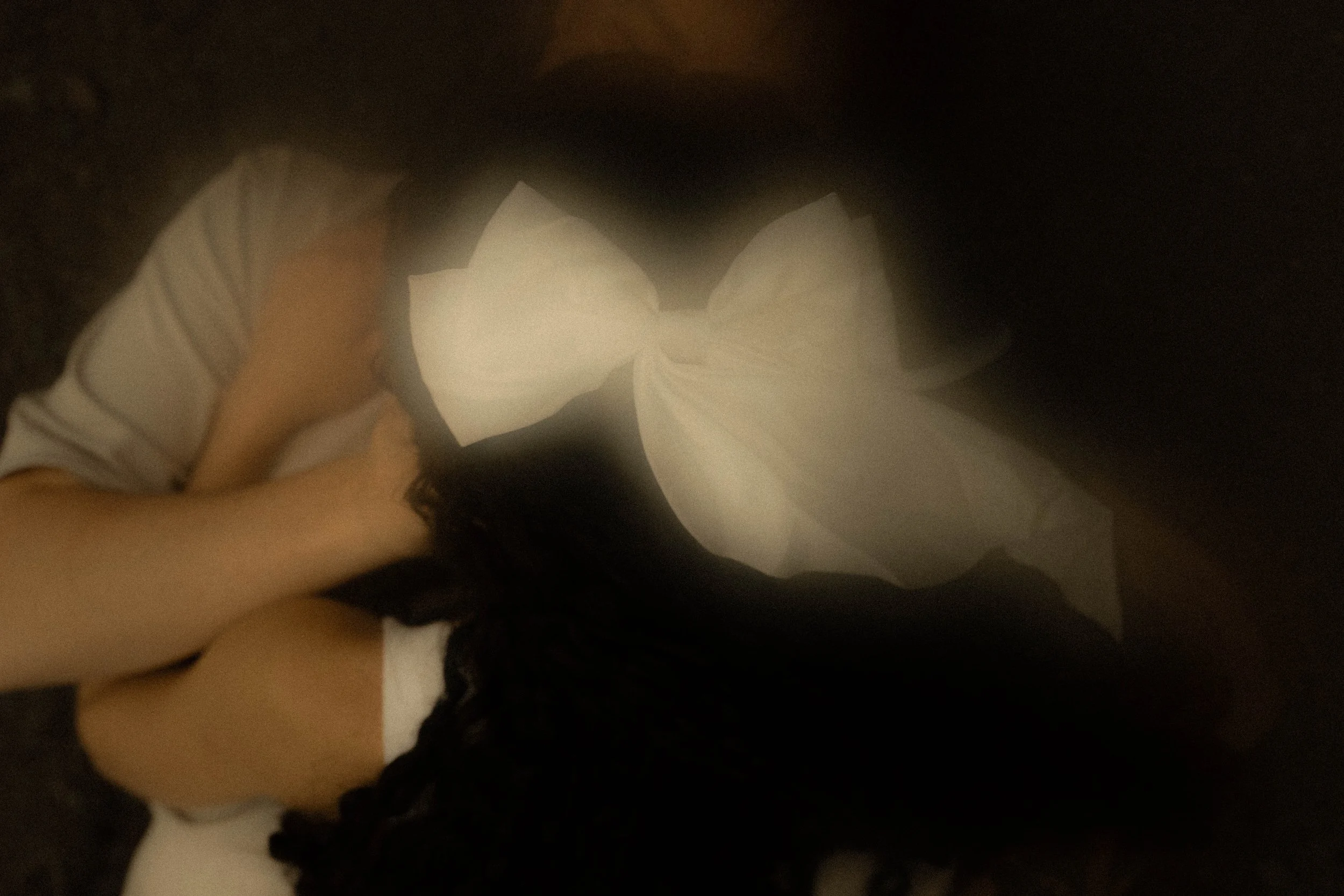 Une personne avec de longs cheveux foncés porte une robe ou un vêtement blanc, dans un endroit sombre ou avec un éclairage faible.