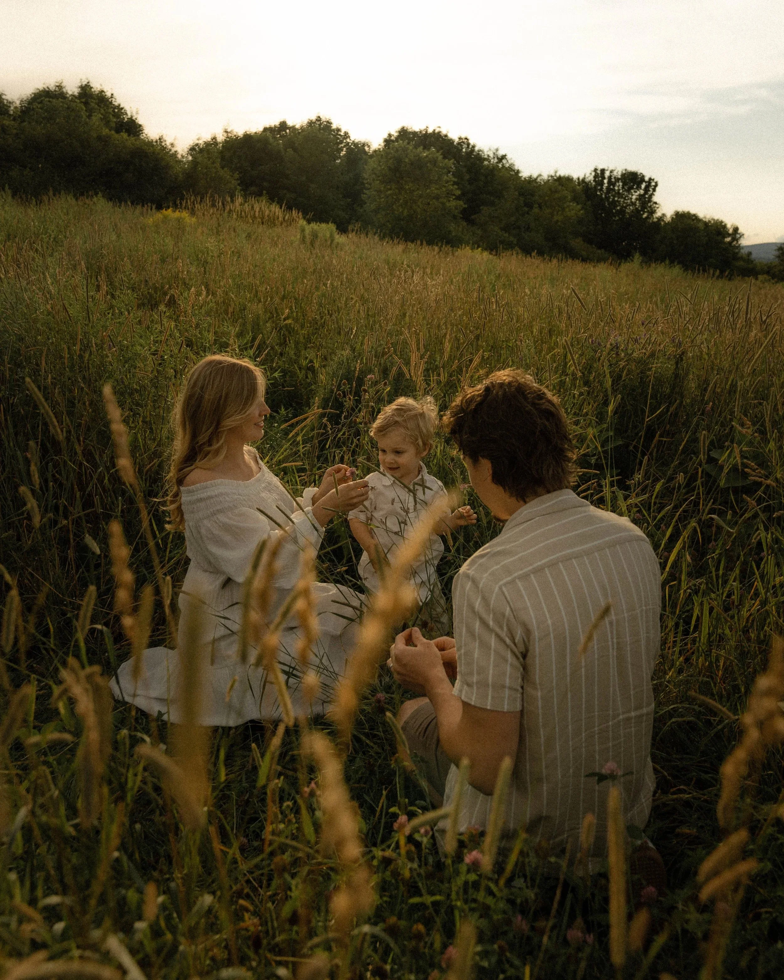 Un groupe de personnes, dont trois enfants, se tient dans un champ d'herbes hautes lors du coucher du soleil, avec des arbres en arrière-plan.
