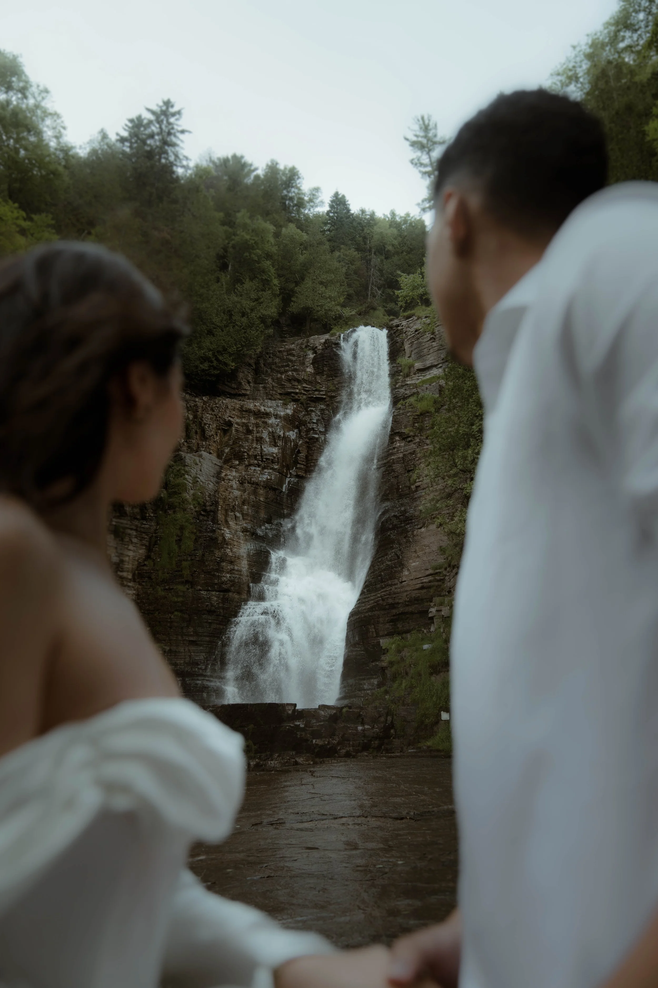 Deux personnes, un homme et une femme, regardent une cascade entourée de forêt dense.