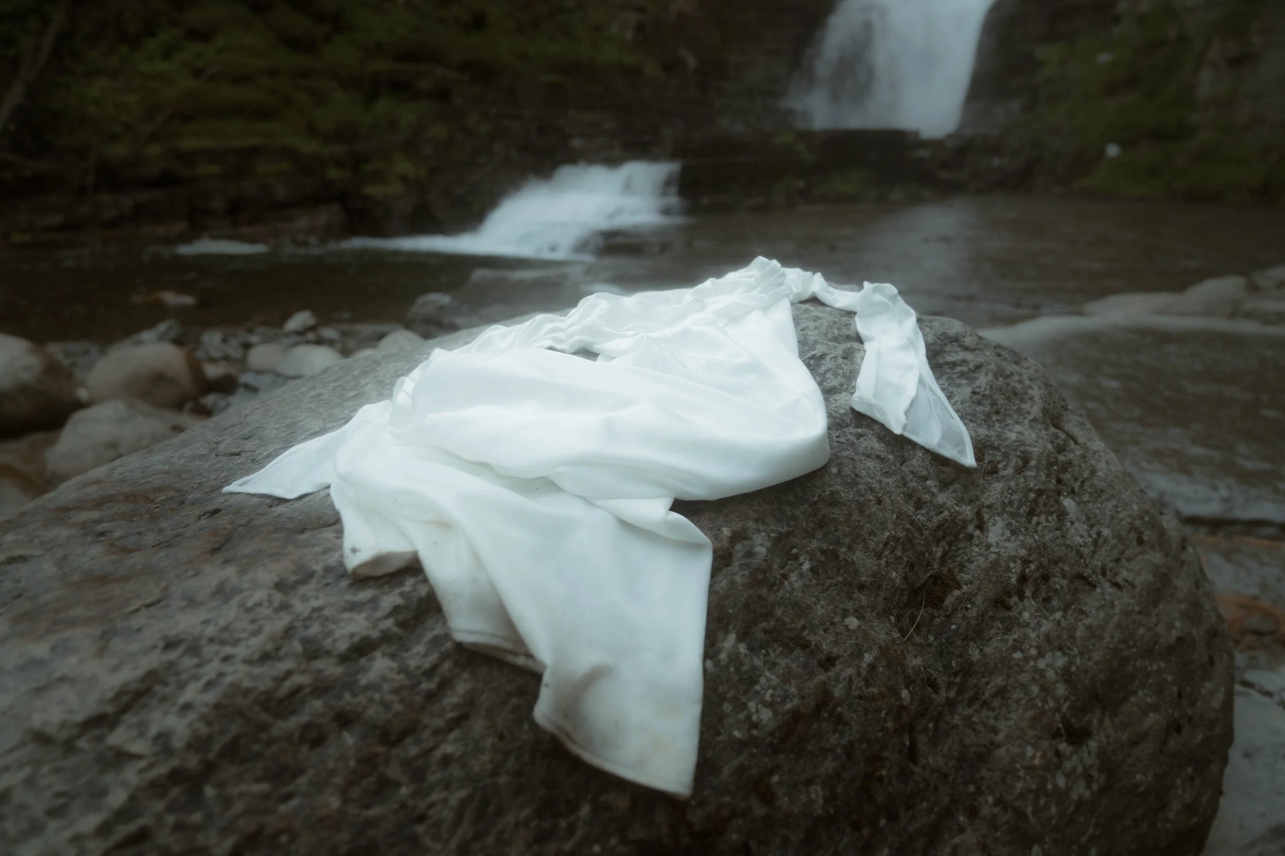 Un tissu blanc déployé sur une roche près d'une rivière avec une cascade en arrière-plan.