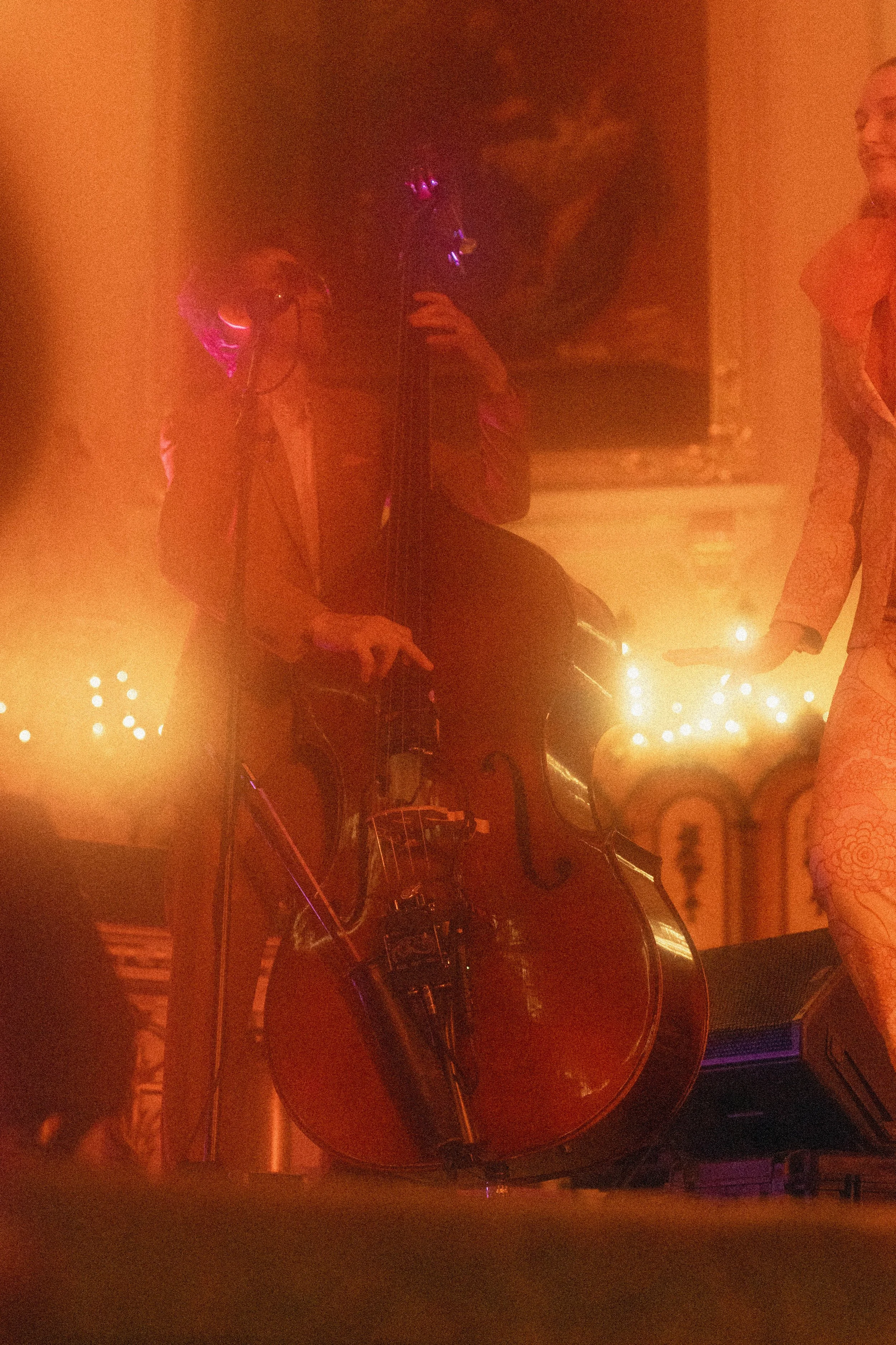 Une personne joue de la guitare électrique dans un lieu sombre, éclairé par une lumière orange chaude, avec un décor de style vintage ou de chambre d'hôtel, et un tableau noir en arrière-plan.