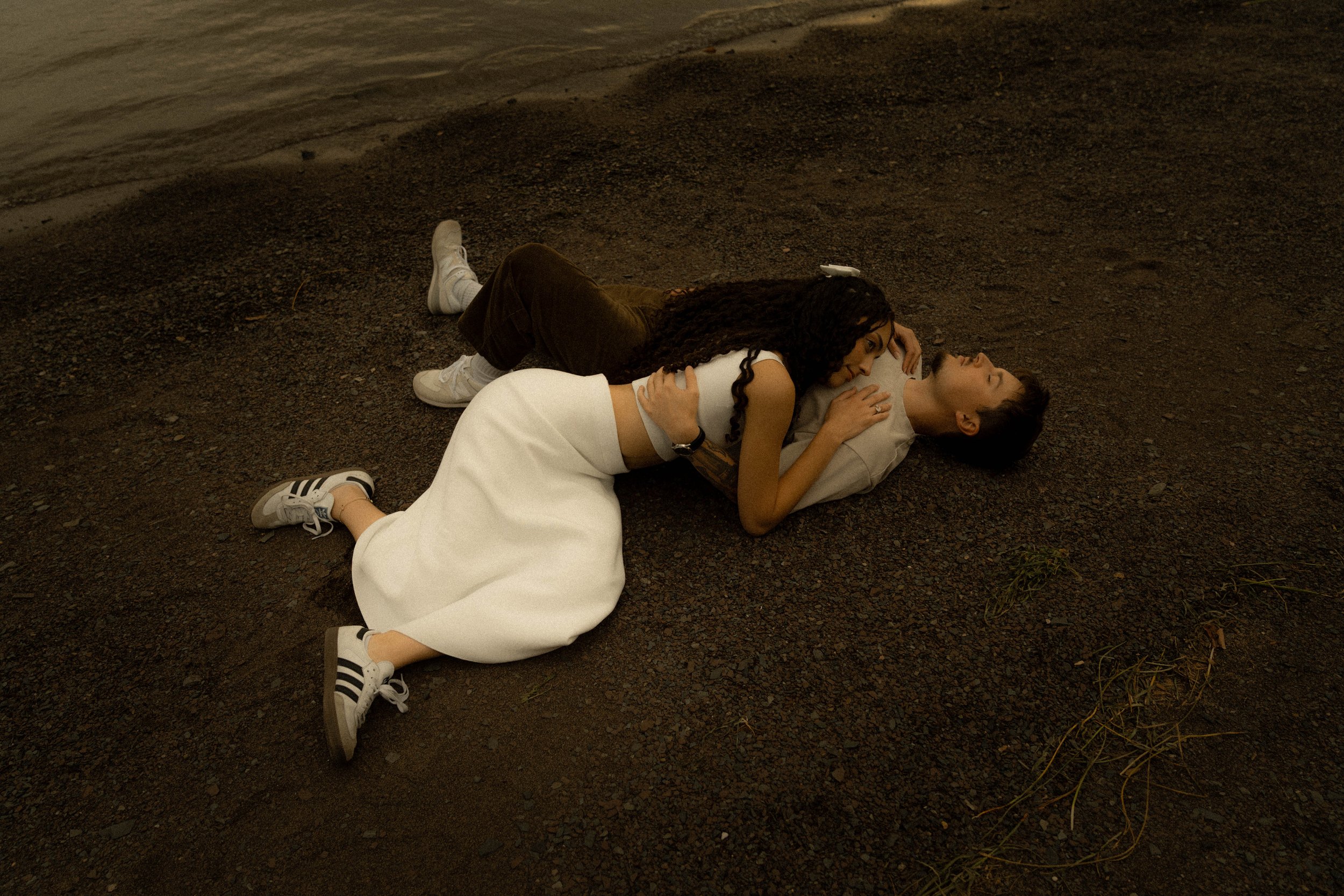 Deux jeunes femmes allongées sur le sol près de l'eau, se regardant et se tenant par la main dans un cadre naturel au coucher du soleil.